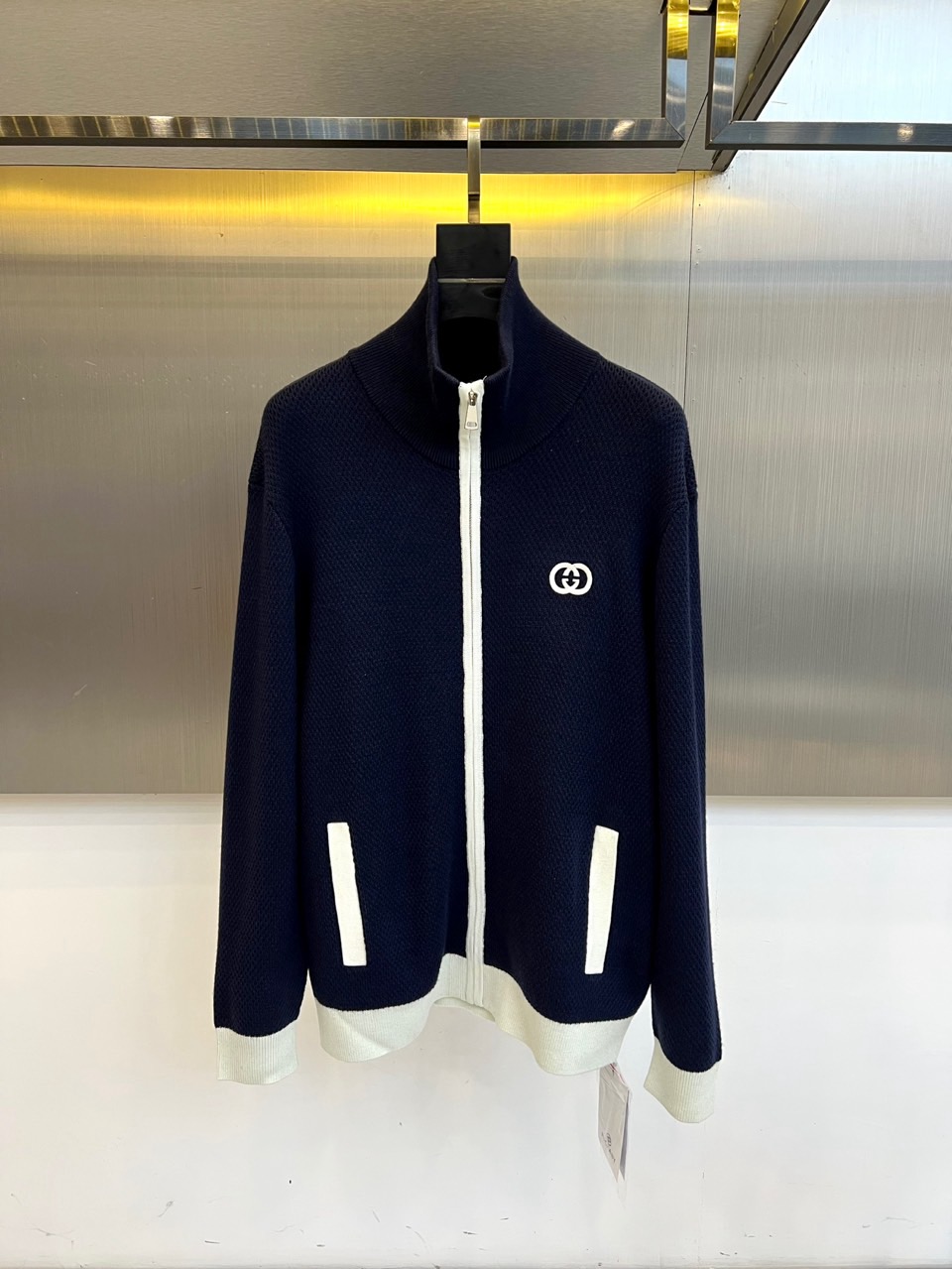 NO:600861,Gucc Gucci (high-end customization),  The new 2025 autumn and winter wool knitted cardigan uses a dark blue and white splicing design to interpret retro-modern aesthetics. The style adopts a stand-up collar design with a white zipper opening and closing system. The collar, cuffs and hem are sharply contrasted with the dark blue body through precise white ribbing.  Contrast. The left chest is embellished with the iconic interlocking G letter badge, and the body is covered with a delicate plaid knitted texture. The fabric combines a golden ratio of 48.4 sheep wool and 51.6 acrylic, which not only retains the natural texture of wool, but also uses acrylic to enhance the stability of the silhouette.  Its design combines the brand's classic genes with sports style. It can be worn with a white T-shirt to create a layered look, or it can be worn alone with casual pants to show a lazy style. From art exhibitions to weekend parties, this cardigan has become a fashion carrier that connects retro aesthetics and contemporary life with its nautical-inspired color collision, precise tailoring technology and first-class exquisite workmanship. Strictly implement FZ/T  73018-Industry standards and Class B safety regulations, interpreting Gucci’s exploration of the innovative boundaries of knitted items. 48-56 (model weighs 173,143 pounds, upper body size 50),,gucci,gucci,tees,t-shirt,gold,alexander wang19860909Gucc古驰（高端定制）、 2025秋冬新品羊毛针织开衫,以深蓝与白色拼接设计演绎复古摩登美学.款式采用立领设计搭配白色拉链开合系统,领口、袖口及下摆通过精准的白色罗纹收边与深蓝衣身形成鲜明对比.左胸点缀标志性互扣式G字母徽章,衣身满铺细腻的格纹针织纹理,面料融合48.4绵羊毛与51.6腈纶的黄金配比,既保留羊毛的天然质感,又通过腈纶增强廓形稳定性. 其设计将品牌经典基因与运动风格相融合,可内搭白色T恤打造层次感造型,亦可单独搭配休闲裤展现慵懒风尚.从艺术展览到周末聚会,这款开衫以航海灵感的色彩碰撞、精准的剪裁工艺与一等品级的精湛做工,成为连接复古美学与当代生活的时尚载体.严格执行FZ/T 73018-行业标准与B类安全规范,诠释Gucci对针织单品创新边界的探索.48-56（模特173,143斤上身50码）,,gucci,gucci,tees，t-shirt,gold,alexander wang,Men's clothing