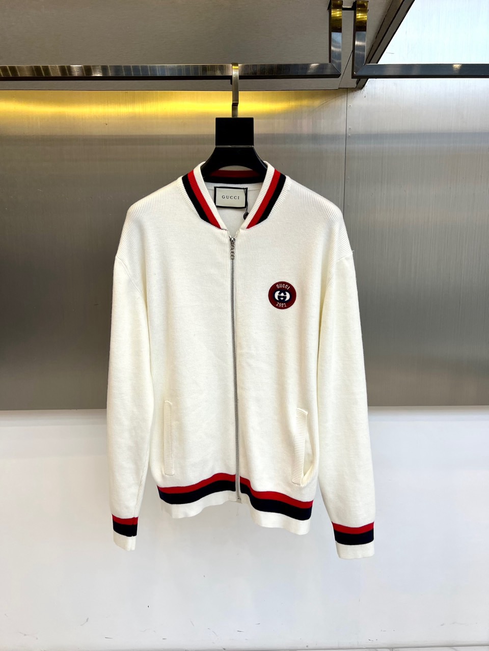 NO:608678,Gucci, 2025 autumn and winter new knitted jacket, this zippered jacket is made of cotton fabric, decorated with red and black contrasting stripes on the collar, cuffs and hem. The left chest is embellished with the brand's iconic circular badge, embroidered with the GUCCI logo and '1921' heritage year. Three-dimensional tailoring with a slightly loose fit, and ribbed trimming technology ensures that the silhouette remains neat. Its design perfectly blends sports elements with Italian sophistication, and the pure white background is eye-catching.  The logo can be paired with casual pants to create a daily look, or it can be combined with formal pants to create a mixed style. The label clearly indicates professional care guidelines, and it is recommended to wash and iron on the inside. From urban leisure to social occasions, this jacket has become a must-have item in the autumn and winter wardrobe with both practicality and brand recognition with exquisite craftsmanship and iconic design. 48-56 (please state your height and weight when placing an order),, gucci, gucci, jackets  & coats,alexander wang19860909Gucc古驰、2025秋冬新品针织外套,这款拉链开合外套采用棉质面料,领口、袖口及下摆处饰以红黑对比条纹,左胸点缀品牌标志性圆形徽章,绣有GUCCI标识与'1921'传承年份.立体剪裁配合微宽松版型,罗纹收边工艺确保廓形保持利落.其设计将运动元素与意式精致完美融合,纯白底色搭配醒目标识,既可搭配休闲裤打造日常造型,也能与正装裤碰撞出混搭风格.标签明确标注专业护理指南,建议反面洗涤与熨烫.从都市休闲到社交场合,这件外套以精湛工艺与标志性设计,成为秋冬衣橱中兼具实穿性与品牌辨识度的必备单品.48-56（下单请报身高体重）,,gucci,gucci,jackets & coats,alexander wang,Men's clothing