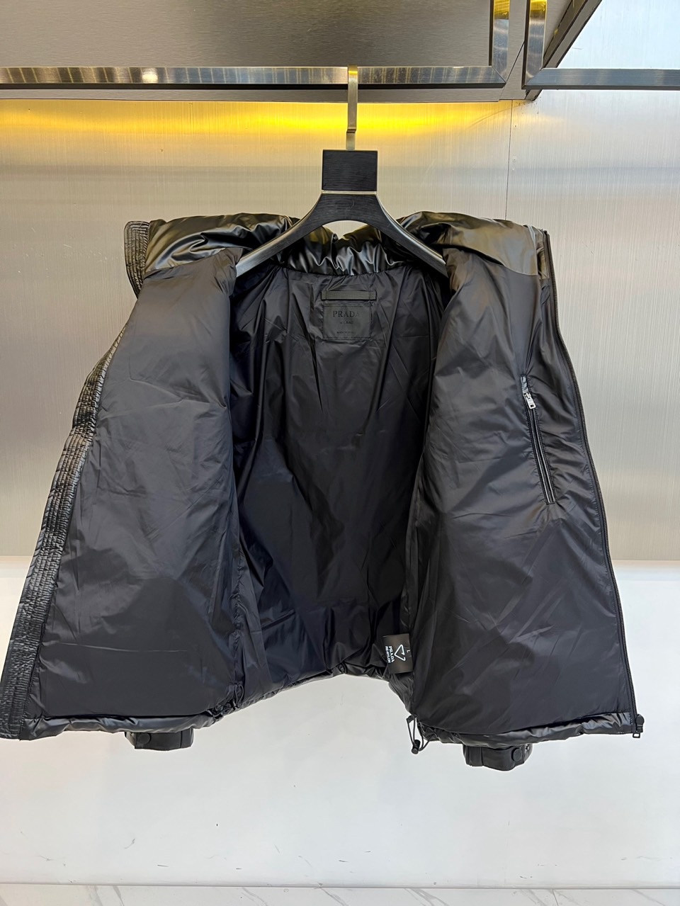 Prad普拉达、2025秋冬新款羽绒服，以纯黑配色演绎意式极简美学。这款连帽羽绒服采用宽松立体剪裁，衣身