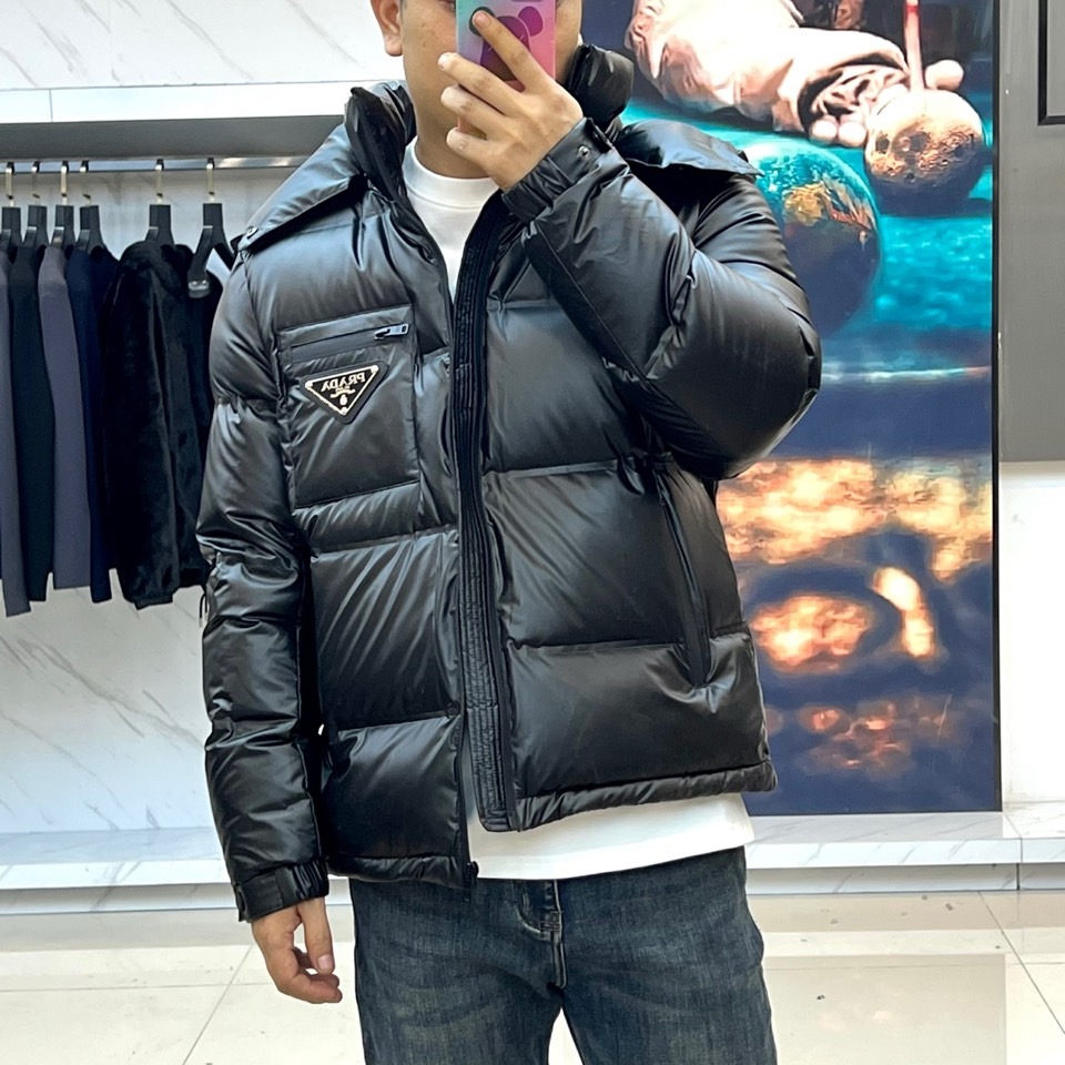 Prad普拉达、2025秋冬新款羽绒服，以纯黑配色演绎意式极简美学。这款连帽羽绒服采用宽松立体剪裁，衣身