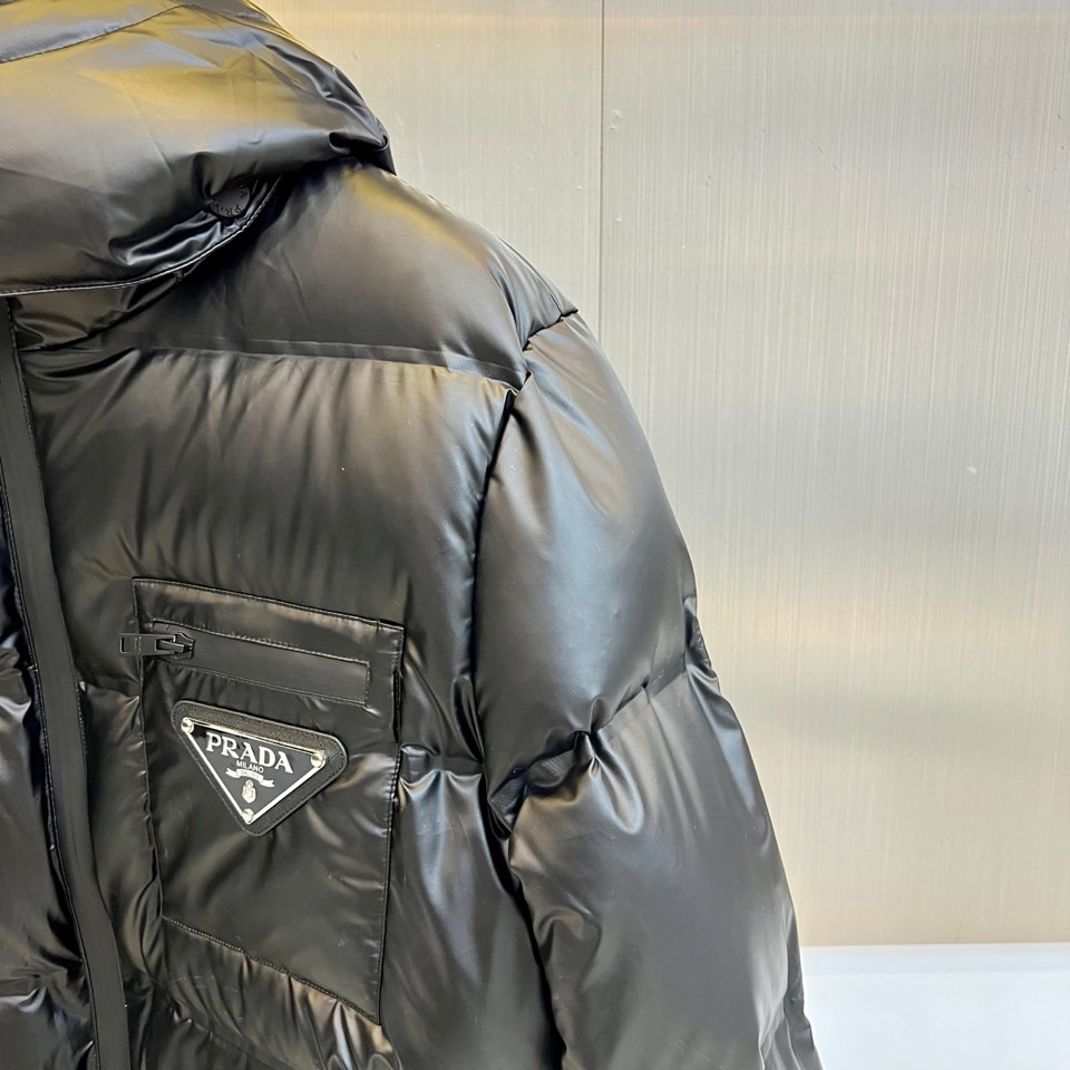 Prad普拉达、2025秋冬新款羽绒服，以纯黑配色演绎意式极简美学。这款连帽羽绒服采用宽松立体剪裁，衣身