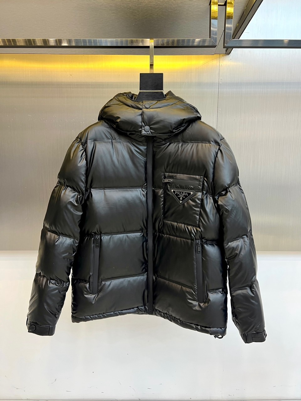Prad普拉达、2025秋冬新款羽绒服，以纯黑配色演绎意式极简美学。这款连帽羽绒服采用宽松立体剪裁，衣身