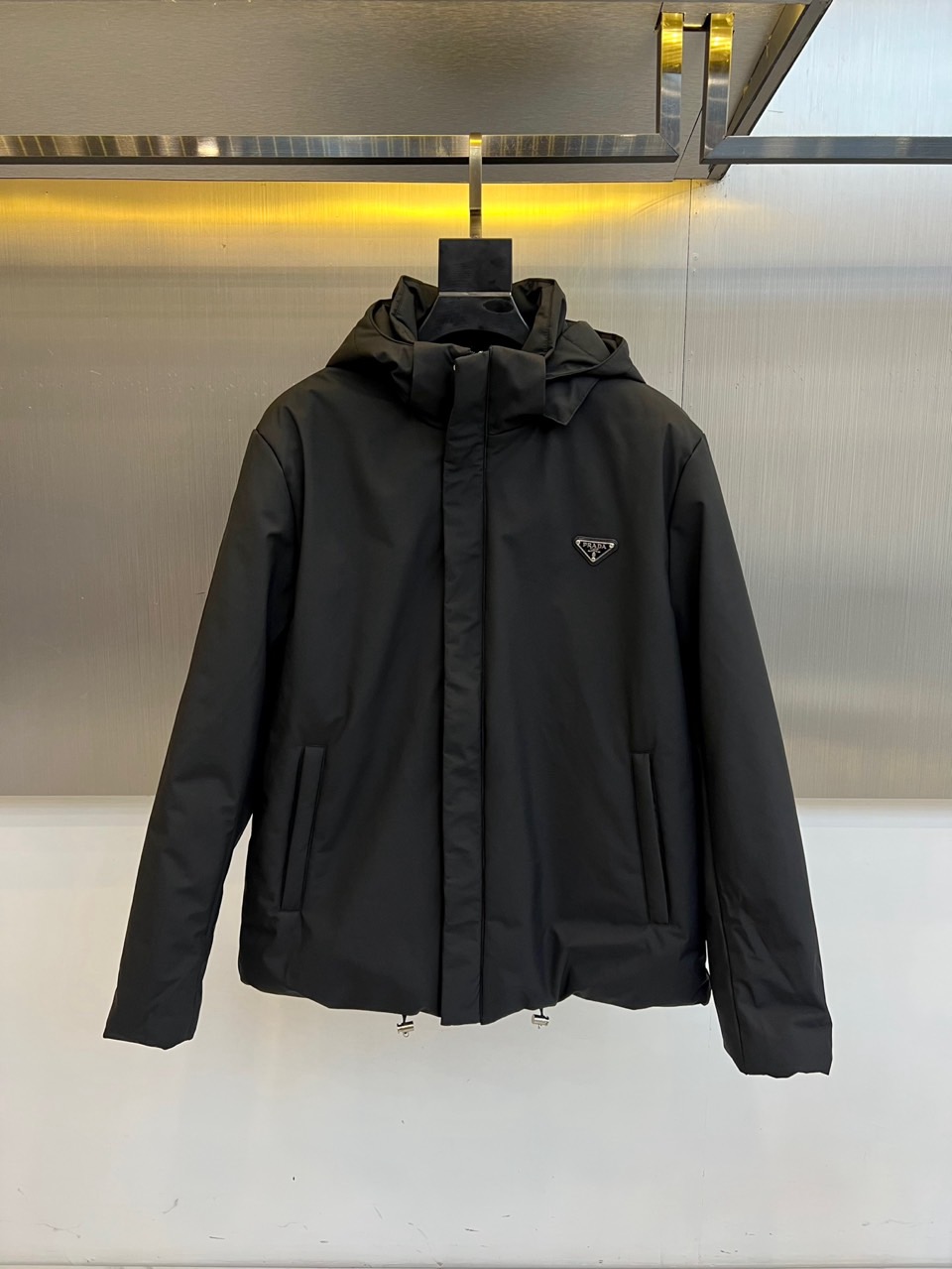 Prad普拉达、2025秋冬新款棉服以深邃藏蓝色演绎都市实用美学。这款连帽棉服采用立体绗缝工艺形成规整的