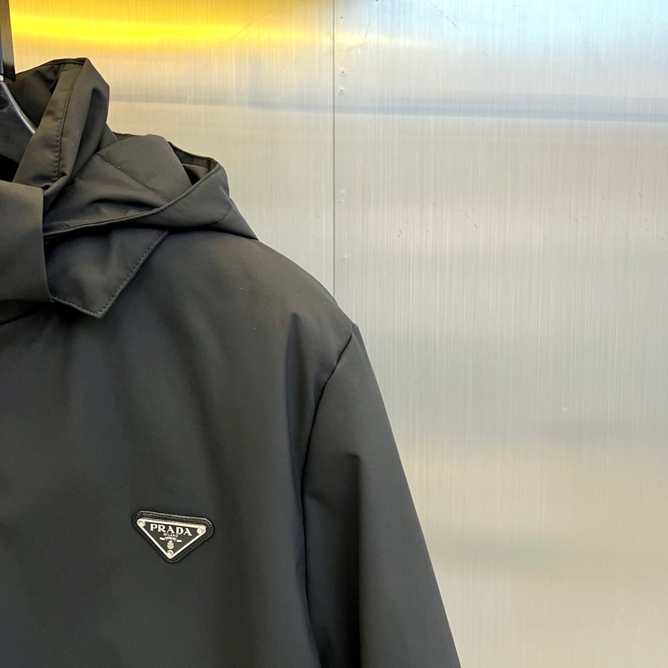 Prad普拉达、2025秋冬新款棉服以深邃藏蓝色演绎都市实用美学。这款连帽棉服采用立体绗缝工艺形成规整的