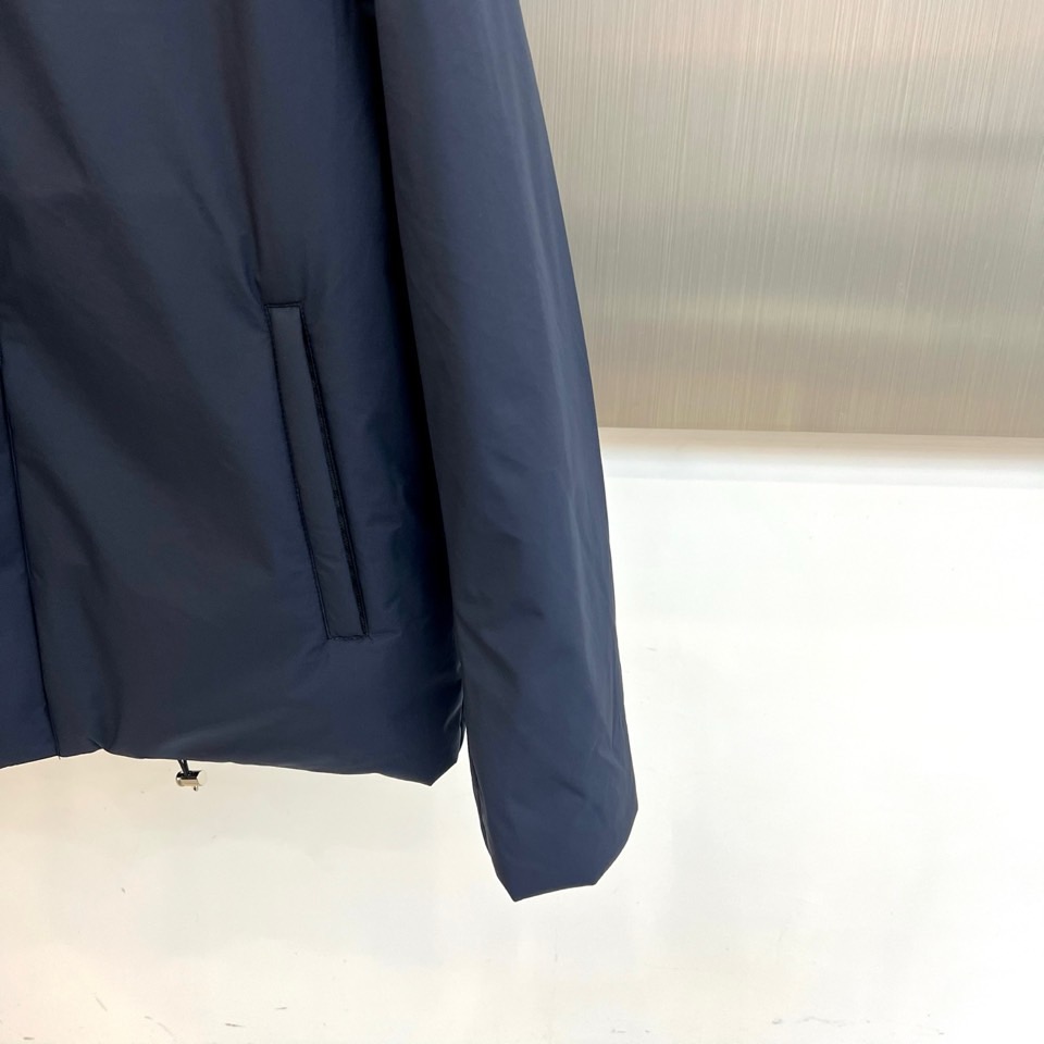 Prad普拉达、2025秋冬新款棉服以深邃藏蓝色演绎都市实用美学。这款连帽棉服采用立体绗缝工艺形成规整的