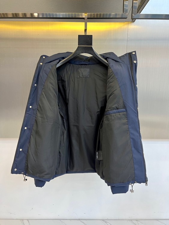 Prad普拉达、2025秋冬新款棉服以深邃藏蓝色演绎都市实用美学。这款连帽棉服采用立体绗缝工艺形成规整的