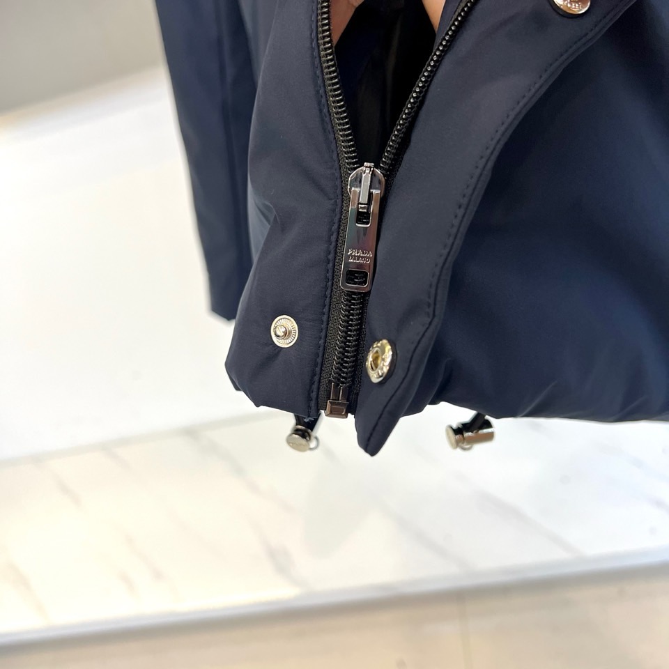 Prad普拉达、2025秋冬新款棉服以深邃藏蓝色演绎都市实用美学。这款连帽棉服采用立体绗缝工艺形成规整的