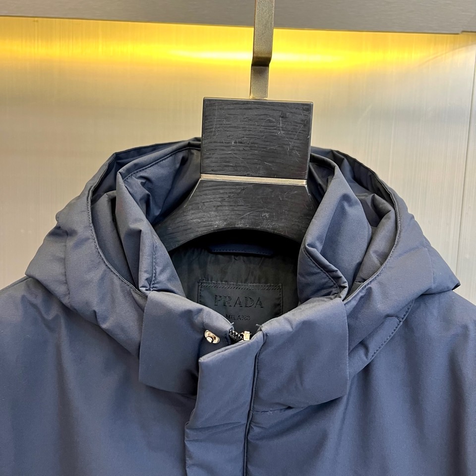 Prad普拉达、2025秋冬新款棉服以深邃藏蓝色演绎都市实用美学。这款连帽棉服采用立体绗缝工艺形成规整的
