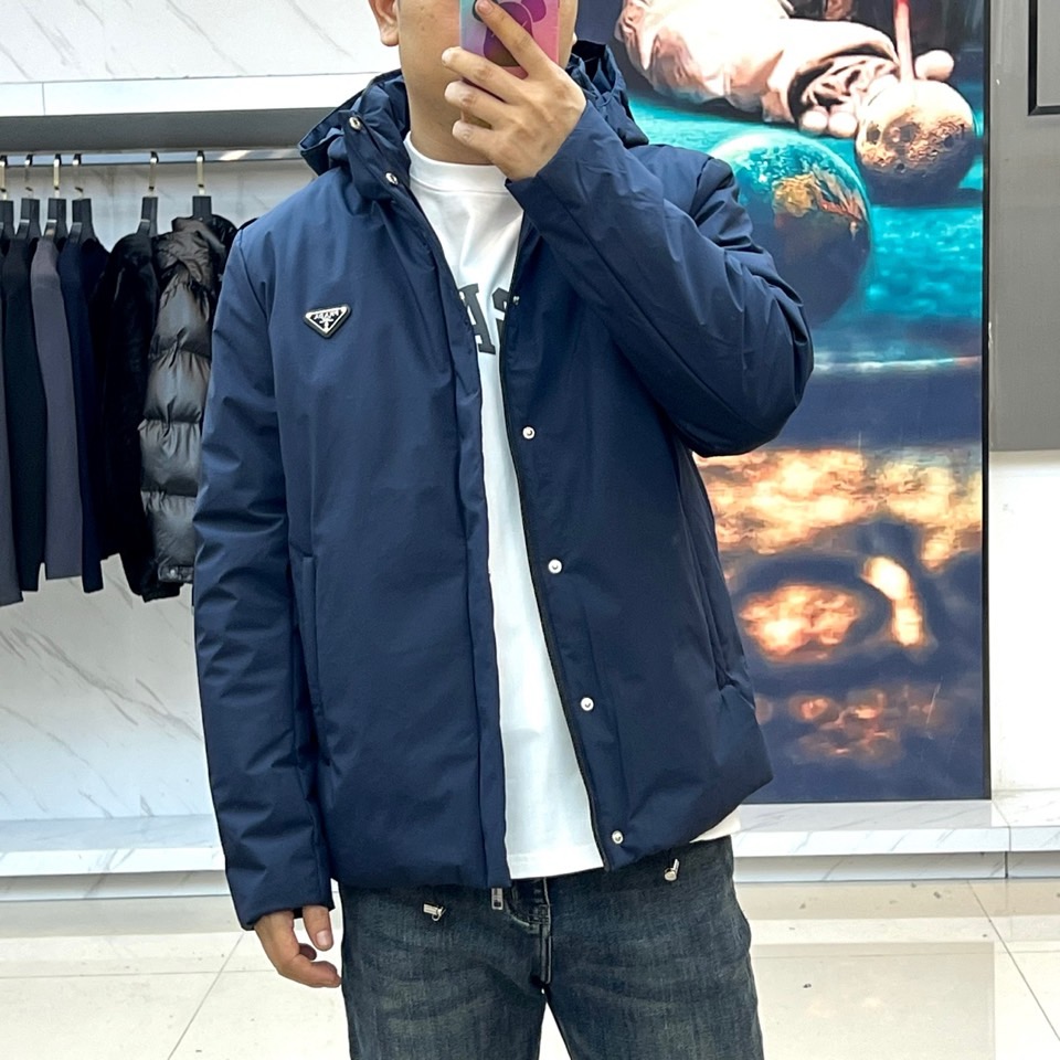 Prad普拉达、2025秋冬新款棉服以深邃藏蓝色演绎都市实用美学。这款连帽棉服采用立体绗缝工艺形成规整的