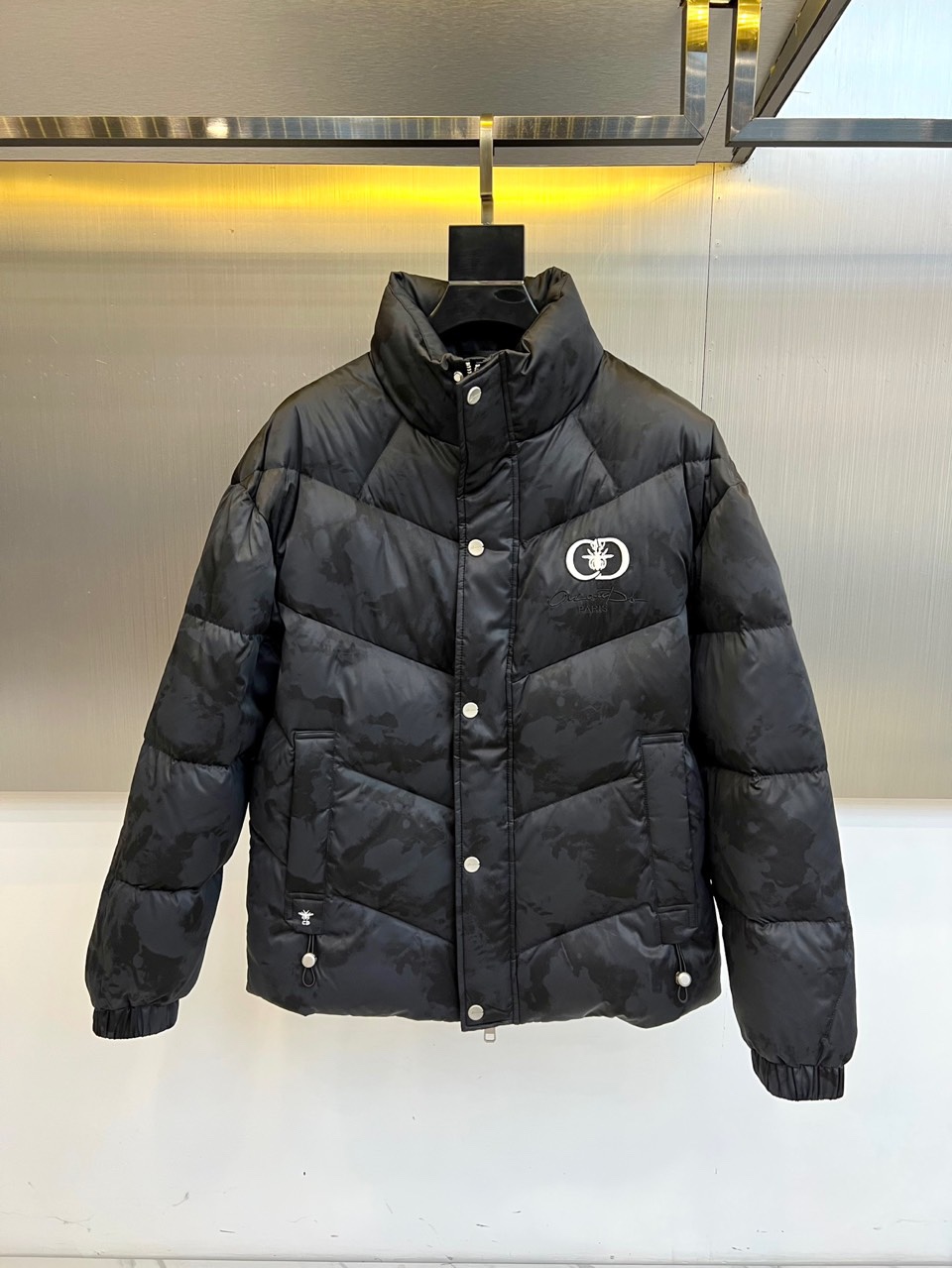 NO:613173,Dio, the new 2025 autumn and winter down jacket, uses classic black to interpret the perfect balance of French elegance and practical functionality. This down jacket adopts a stand-up collar design, with a row of exquisite silver buttons, showing a luxurious texture in a low-key manner. The left chest is decorated with the brand's iconic white double G pattern embroidery, becoming the overall visual focus. The body is made of exquisite rhombus plaid quilting technology to outline a full three-dimensional outline, ensuring that the down is evenly distributed while enhancing the warmth retention performance.  The fabric is made of polyester fiber, which has good windproof performance; the lining is nylon, which provides a comfortable wearing experience. The filling is made of high-quality white duck down with 85% down content, and is matched with 210g of down filling to ensure excellent thermal insulation effect in cold seasons. Practical pockets on both sides and windproof cuffs are designed to take into account both appearance and functionality.  Its design combines Dior's classic aesthetics with winter practical needs. Its slim fit avoids the bloated feel of traditional down jackets. Silver buttons and white embroidery details add exquisite highlights to the overall look. From urban commuting to weekend trips, this down jacket can show the wearer's fashion with a simple yet textured design.  Taste. Every detail reflects the brand's pursuit of quality, including craftsmanship requirements that comply with GB/T14272-standard, making it an ideal choice for autumn and winter wardrobes that combine style and function. 48-56 (model weighs 173,143 pounds, upper body size 50),, dior, dior, down  jacket,alexander wang19860909Dio迪奥、2025秋冬新款羽绒服以经典黑色演绎法式优雅与实用功能的完美平衡.这款羽绒服采用立领设计,搭配一排精致的银色纽扣,在低调中彰显奢华质感.左胸处饰以品牌标志性的白色双G图案刺绣,成为整体的视觉焦点.衣身通过精致的菱形格纹绗缝工艺,勾勒出饱满立体的轮廓,确保羽绒均匀分布的同时增强保暖性能. 面料采用聚酯纤维,具备良好的防风性能；里料为锦纶,提供舒适的穿着体验.填充物选用85绒子含量的优质白鸭绒,搭配210克的充绒量,确保在寒冷季节提供卓越的保暖效果.两侧实用口袋与防风袖口设计,兼顾美观与功能性. 其设计将迪奥的经典美学与冬季实用需求相融合,修身剪裁避免传统羽绒服的臃肿感,银色纽扣与白色刺绣细节为整体造型增添精致亮点.从都市通勤到周末出行,这款羽绒服都能以简约而不失质感的设计,展现穿着者的时尚品味.每一个细节都体现品牌对品质的追求,包括符合GB/T14272-标准的工艺要求,成为秋冬衣橱中兼具风格与功能的理想之选.48-56（模特173,143斤上身50码）,,dior,dior,down jacket,alexander wang,Men's clothing