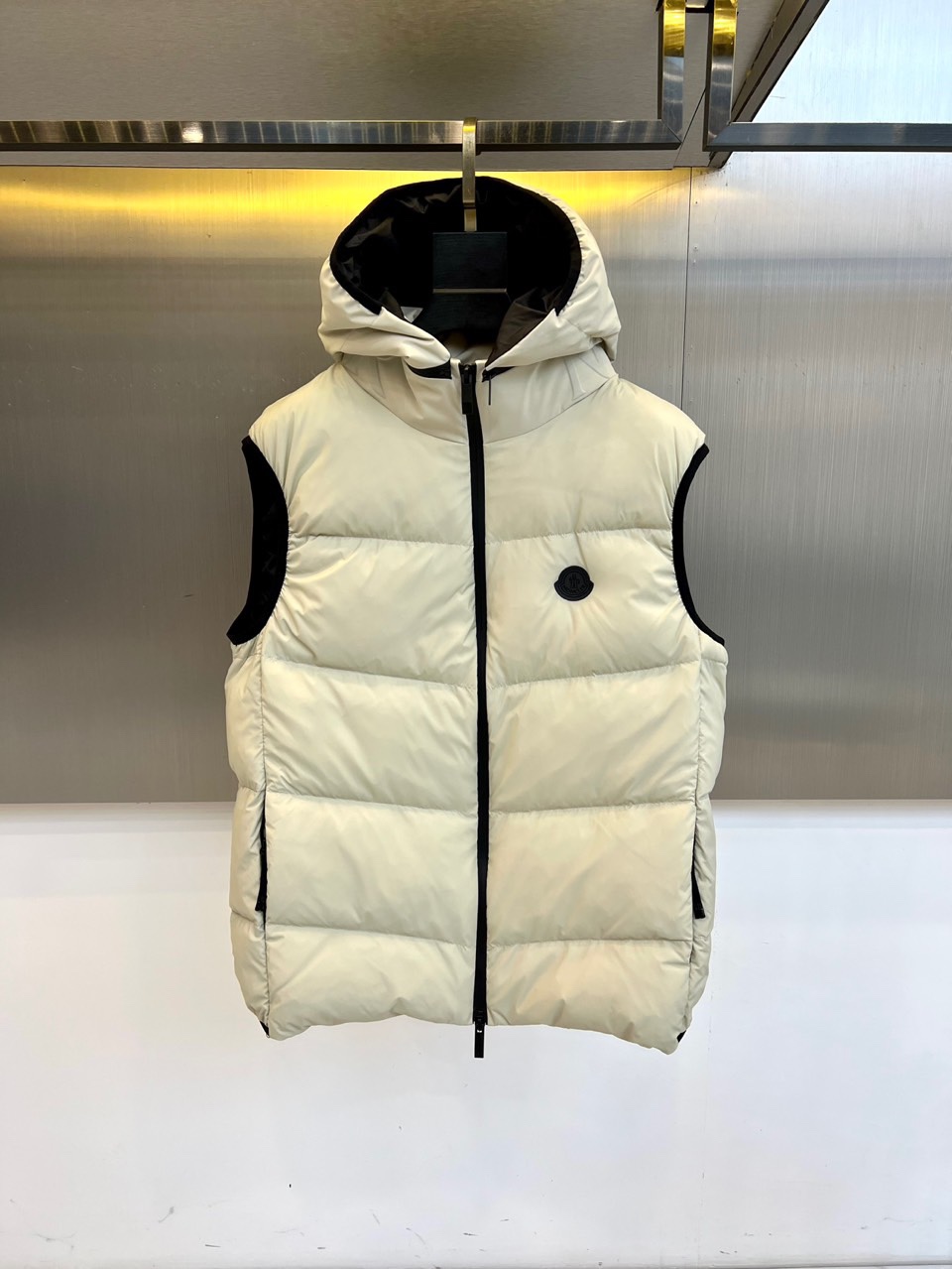 NO:613144,Covered mouth (goose down), 2025 autumn and winter new down vest. This hooded vest is filled with light and warm goose down. The quilting process outlines a regular geometric block outline. The black zipper extends from the hem to the top of the hood, which cleverly echoes the black splicing details at the armholes. The black triangle logo embellished on the left chest shows the brand genes in a low-key manner, and the adjustable brim design enhances practical functions.  Its filling strictly follows the EU EN12934 and USA-double certification standards, using a golden ratio of 90 white goose down and 10 feathers, and the label clearly indicates animal-derived ingredients. The fabric is made of environmentally friendly technology and uses a visual language of black and white contrast to show Prada's unique rational elegance. The straight-cut design leaves ample space for inner wear. It can be paired with a turtleneck sweater to create an urban commuting look, or layered over a suit jacket to create a layered look.  This vest perfectly balances practical functions and fashion expression. The off-white tone gives the winter look a fresh atmosphere, while the black details add visual tension. From walking in the city to outings in the suburbs, it can easily adapt to the needs of a variety of scenes. It not only maintains the thermal properties of down items, but also breaks through the traditional down jackets through neat tailoring.  Thick feeling. Every detail reflects Prada's insistence on materials and craftsmanship, becoming an indispensable and versatile item in the autumn and winter wardrobes of fashionable people who pursue quality life. 48-56 (model weighs 173,143 pounds, upper body size 50),, prada, Moncler, jackets  & coats,down jacket,business suit,gold,hats,alexander wang19860909蒙口（鹅绒）、2025秋冬新品羽绒马甲,这款连帽马甲采用轻盈保暖的鹅绒填充,绗缝工艺勾勒出规整的几何块状轮廓,黑色拉链自下摆延伸至连帽顶端,与袖窿处的黑色拼接细节形成巧妙呼应.左胸点缀的黑色三角徽标低调彰显品牌基因,可调节帽檐设计增强实用功能. 其填充物严格遵循欧盟EN12934与美国USA-双重认证标准,选用90白鹅绒与10羽毛的黄金配比,标签明确标注动物源性成分.面料采用环保科技材质,通过黑白对比的视觉语言展现普拉达特有的理性优雅.直筒版型设计为内搭留出充裕空间,既可搭配高领针织衫打造都市通勤造型,亦可叠穿在西装外套外塑造层次感穿搭. 这款马甲将实用功能与时尚表达完美平衡,米白色调赋予冬季造型清新气息,黑色细节则增添视觉张力.从城市漫步到郊外出行,它能轻松适应多种场景需求,既保持羽绒单品的保暖特性,又通过利落剪裁突破传统羽绒服的厚重感.每一个细节都体现着普拉达对材质与工艺的坚持,成为追求质感生活的时尚人士秋冬衣橱中不可或缺的百搭单品.48-56（模特173,143斤上身50码）,,prada,Moncler,jackets & coats,down jacket,business suit,gold,hats,alexander wang,Men's clothing