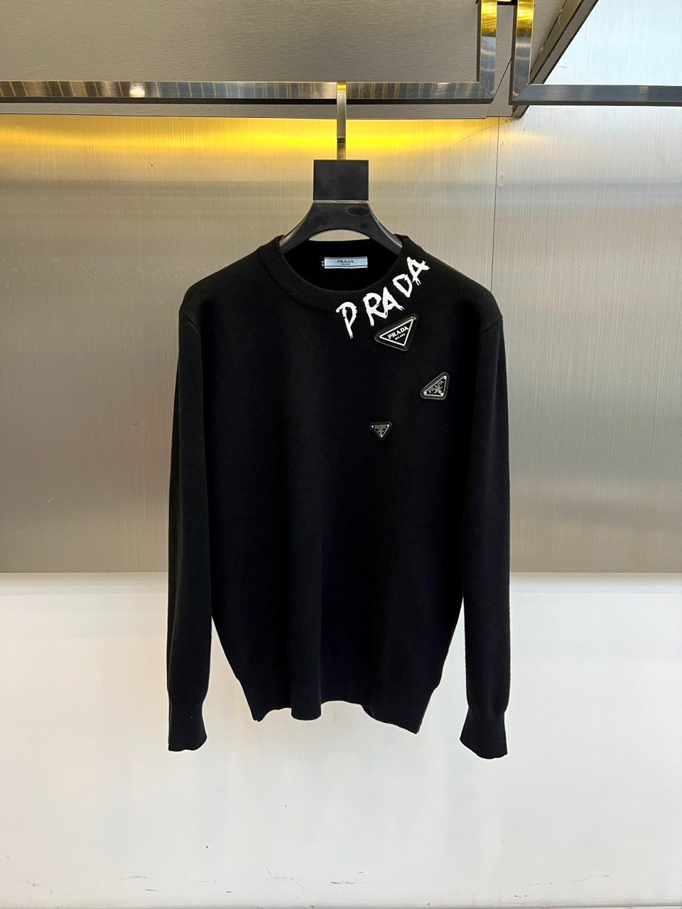 Prad普拉、2025秋冬新品白色针织毛衣，以极简主义美学诠释当代优雅。这款毛衣采用经典圆领设计，左胸位