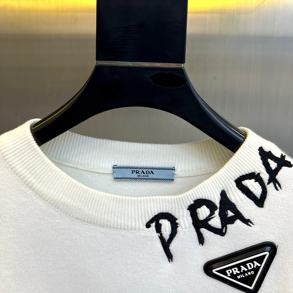 Prad普拉、2025秋冬新品白色针织毛衣，以极简主义美学诠释当代优雅。这款毛衣采用经典圆领设计，左胸位