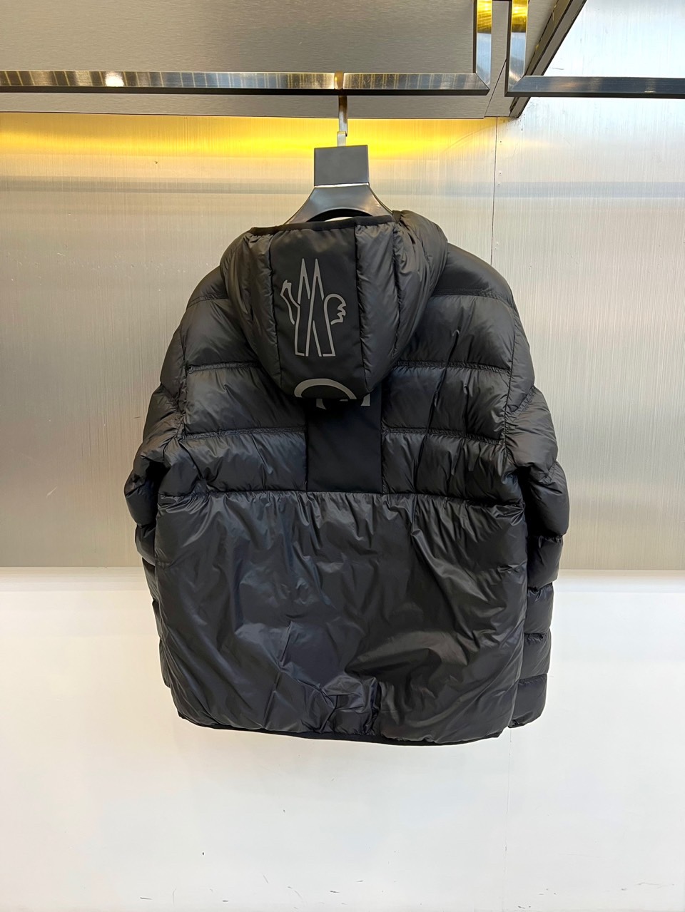 Mon蒙口（纯鹅绒）、2025秋冬新款羽绒服，以经典黑色演绎都市户外美学。这款连帽羽绒服采用横向绗缝工艺