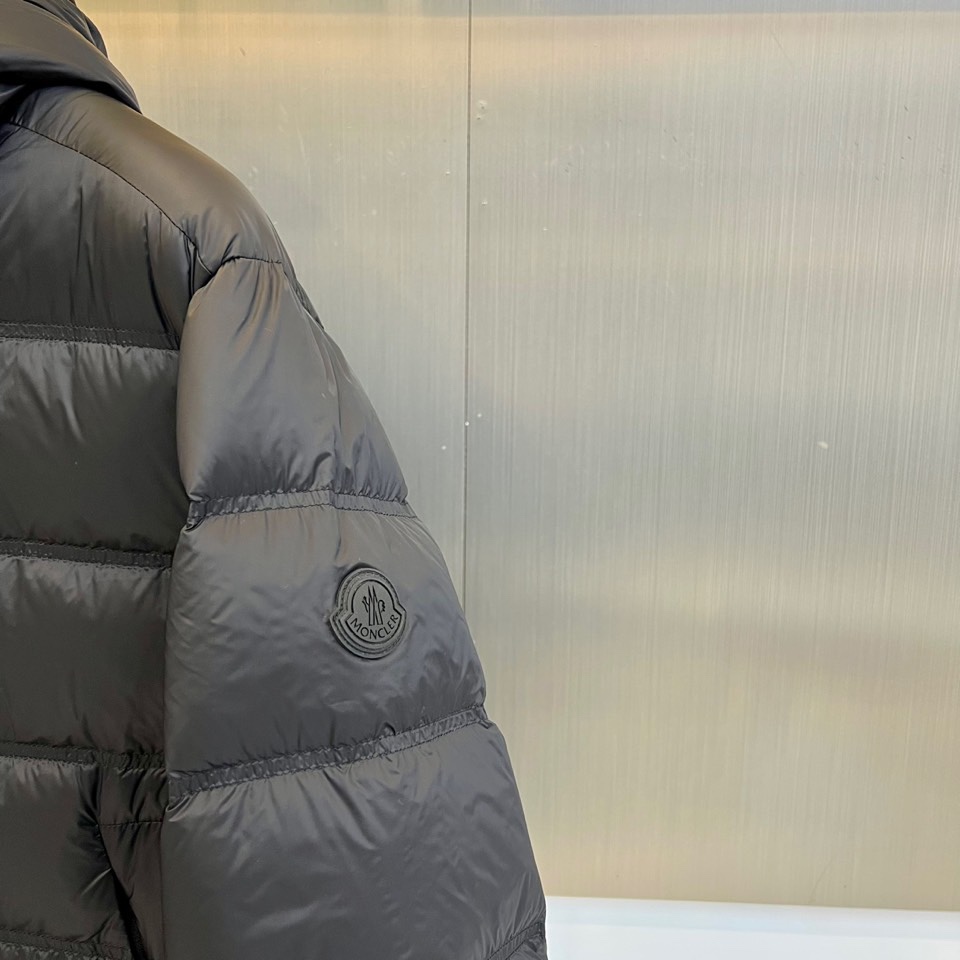 Mon蒙口（纯鹅绒）、2025秋冬新款羽绒服，以经典黑色演绎都市户外美学。这款连帽羽绒服采用横向绗缝工艺