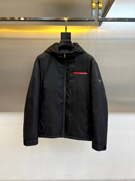 Prad普拉、2025秋冬新品 PRADA科技防护羽绒服。深蓝色连帽设计搭配精密拉链系统，左胸红色织带镶