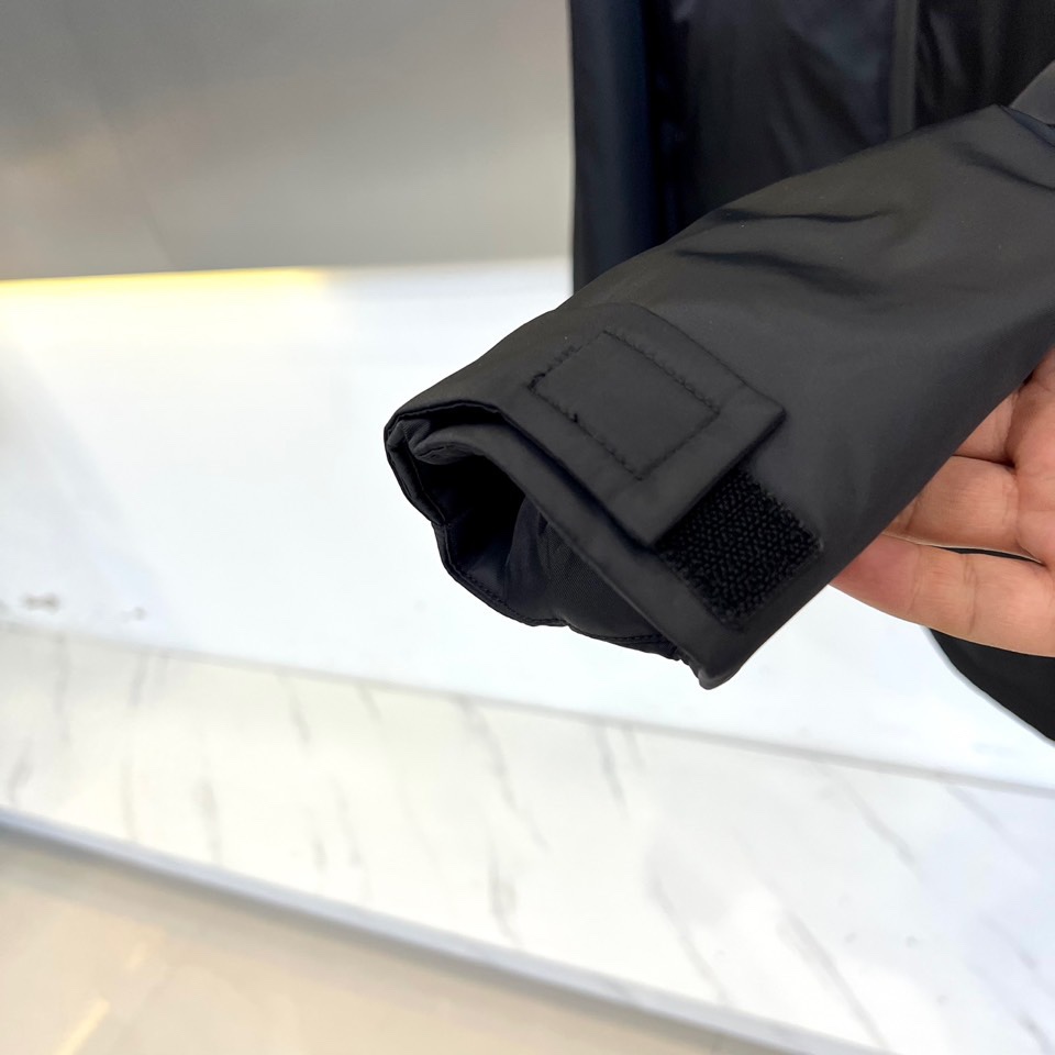 Prad普拉、2025秋冬新品 PRADA科技防护羽绒服。深蓝色连帽设计搭配精密拉链系统，左胸红色织带镶