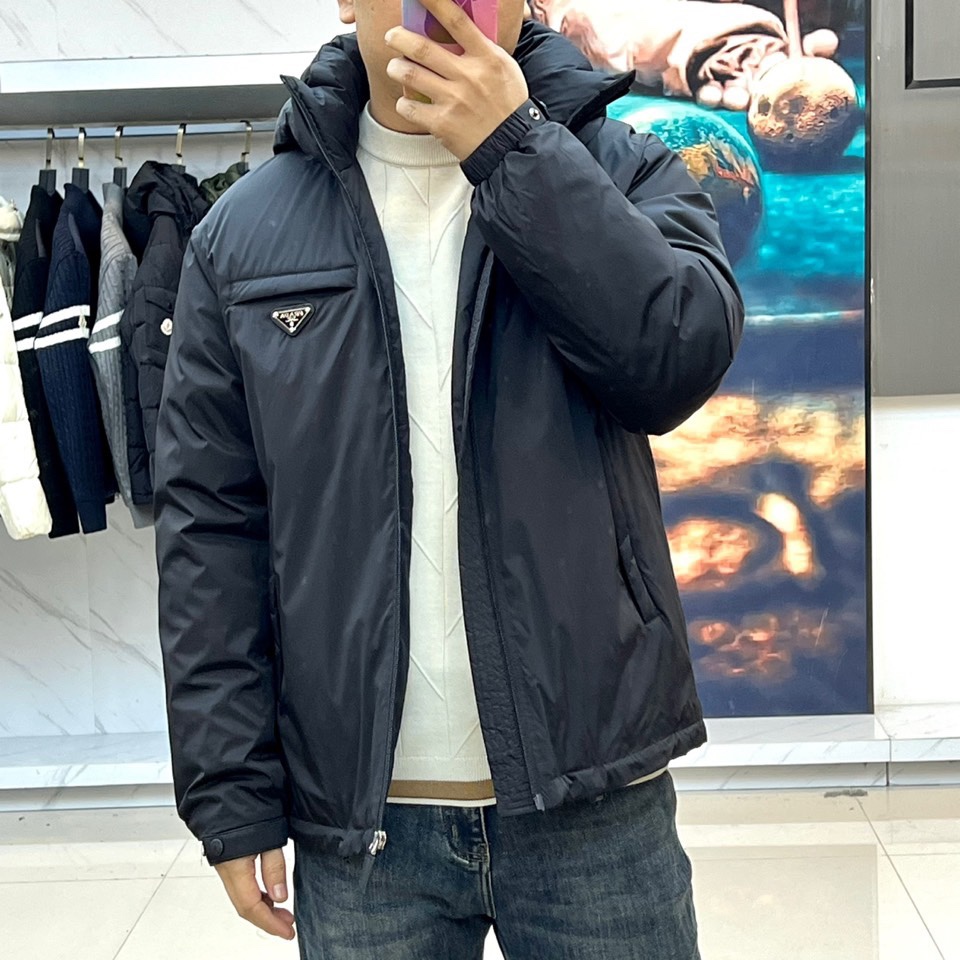 \nPrad普拉达、2025秋冬新款羽绒服，以经典黑色演绎意式极简美学。这款连帽羽绒服采用立体菱形绗缝工