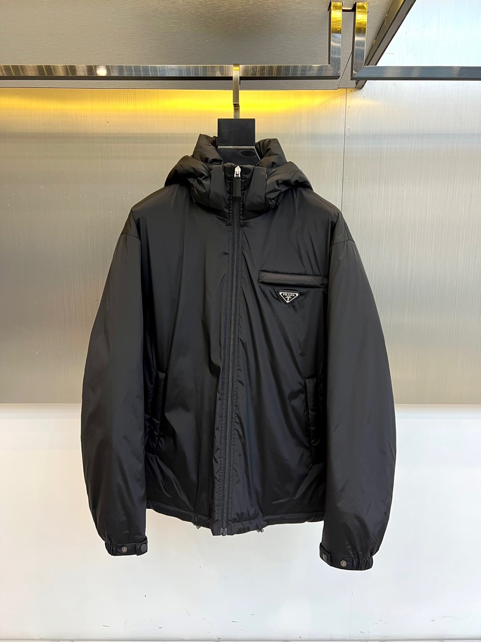 \nPrad普拉达、2025秋冬新款羽绒服，以经典黑色演绎意式极简美学。这款连帽羽绒服采用立体菱形绗缝工