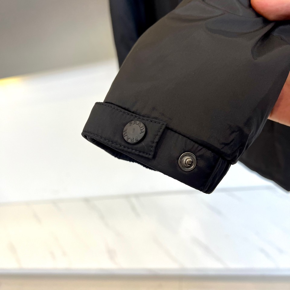 \nPrad普拉达、2025秋冬新款羽绒服，以经典黑色演绎意式极简美学。这款连帽羽绒服采用立体菱形绗缝工