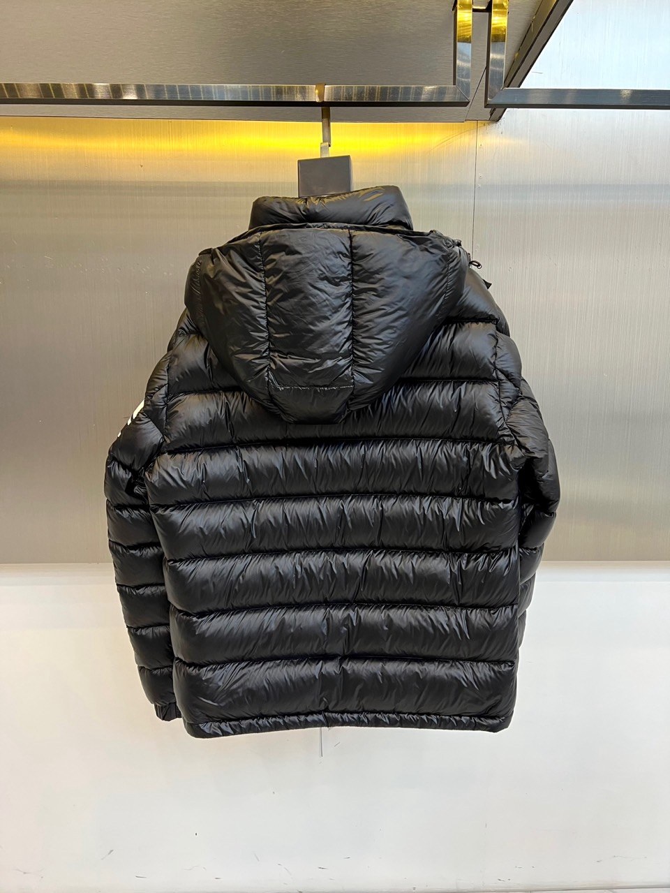 Mon蒙口、2025秋冬新品羽绒服，连帽设计搭配顺滑拉链开合，左臂饰有品牌标志性黑白条纹织带与浮雕徽章，