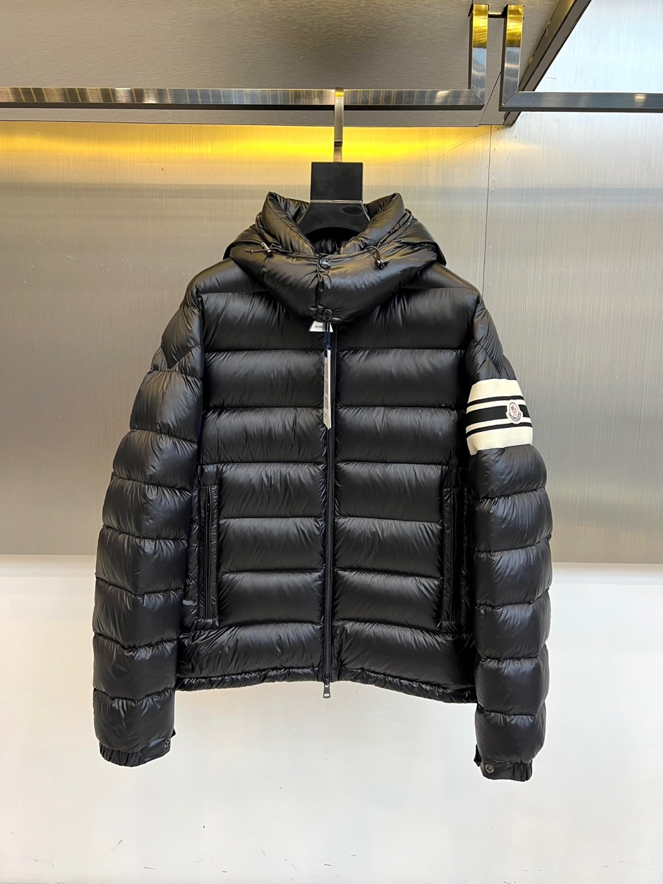 Mon蒙口、2025秋冬新品羽绒服，连帽设计搭配顺滑拉链开合，左臂饰有品牌标志性黑白条纹织带与浮雕徽章，