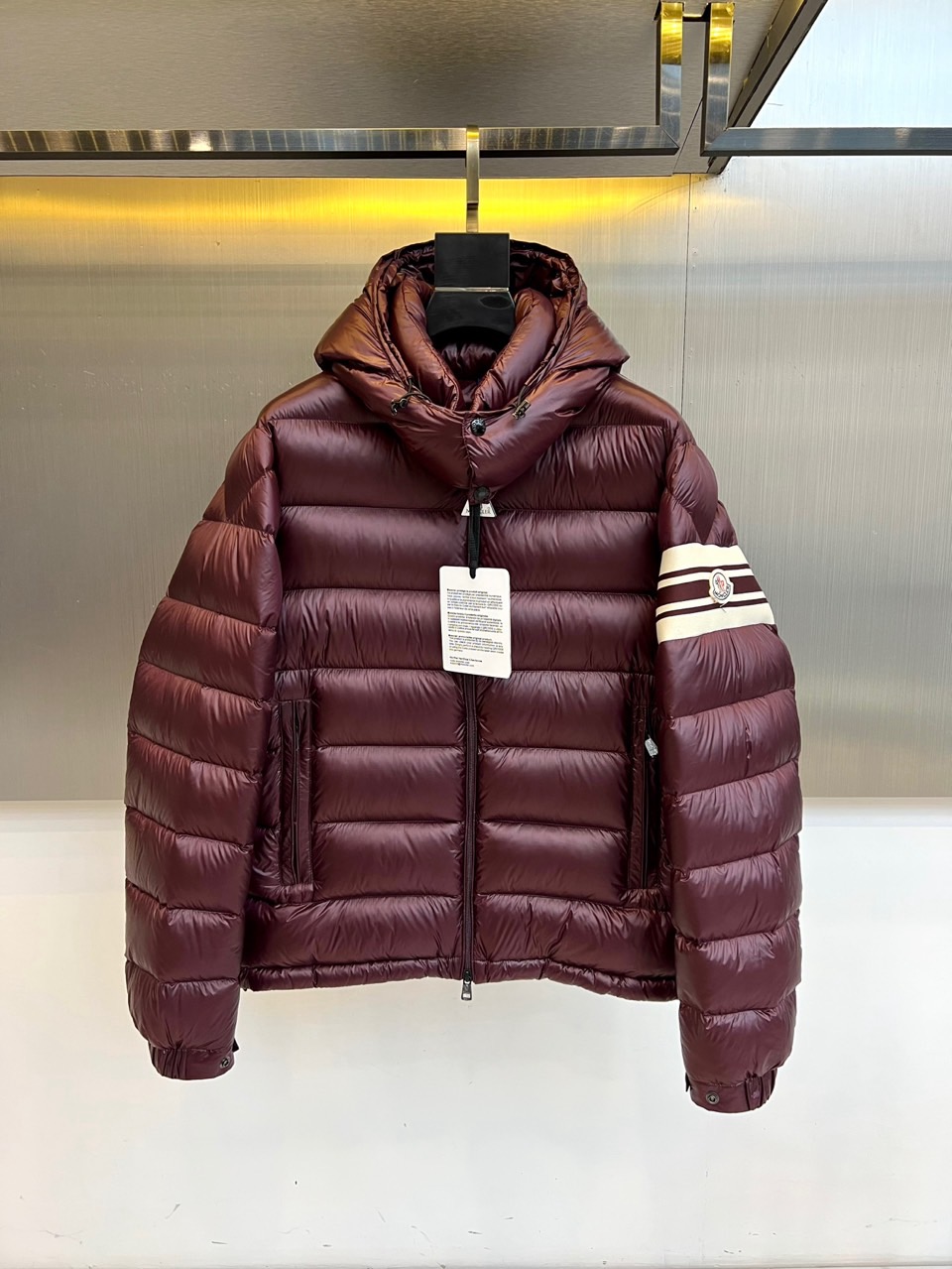 Mon蒙口、2025秋冬新品羽绒服，连帽设计搭配顺滑拉链开合，左臂饰有品牌标志性黑白条纹织带与浮雕徽章，