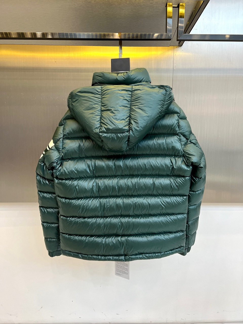 Mon蒙口、2025秋冬新品羽绒服，连帽设计搭配顺滑拉链开合，左臂饰有品牌标志性黑白条纹织带与浮雕徽章，