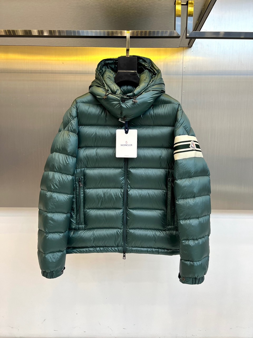 Mon蒙口、2025秋冬新品羽绒服，连帽设计搭配顺滑拉链开合，左臂饰有品牌标志性黑白条纹织带与浮雕徽章，