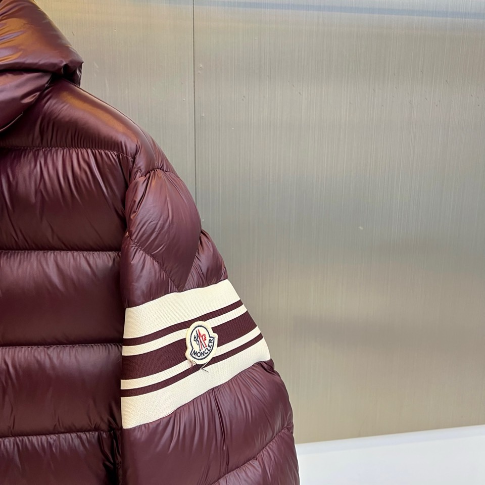 Mon蒙口、2025秋冬新品羽绒服，连帽设计搭配顺滑拉链开合，左臂饰有品牌标志性黑白条纹织带与浮雕徽章，