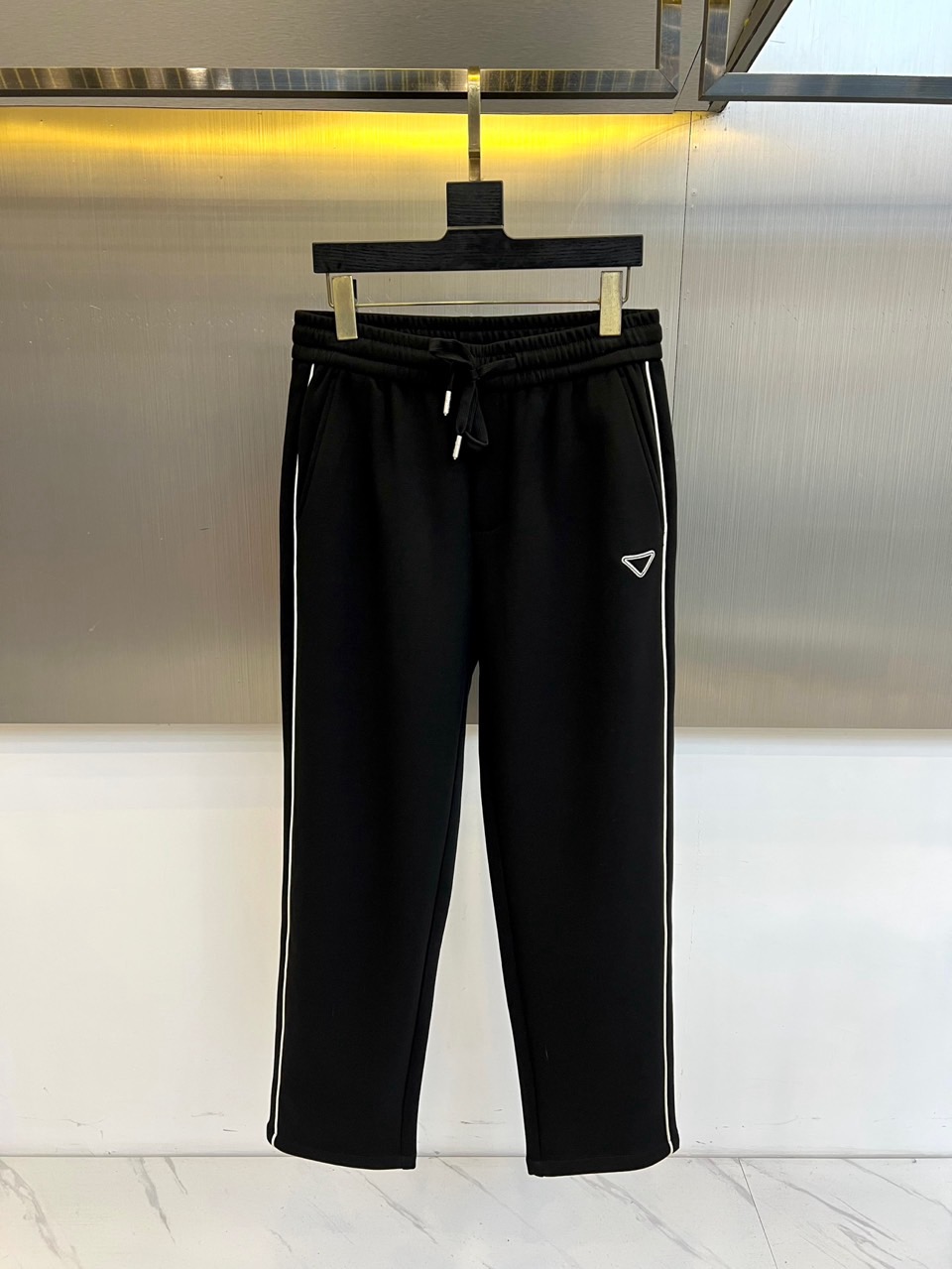 Prad普拉、2025秋冬新品运动长裤，以标志性设计语言诠释现代休闲美学。款式采用弹性抽绳腰头设计，两侧