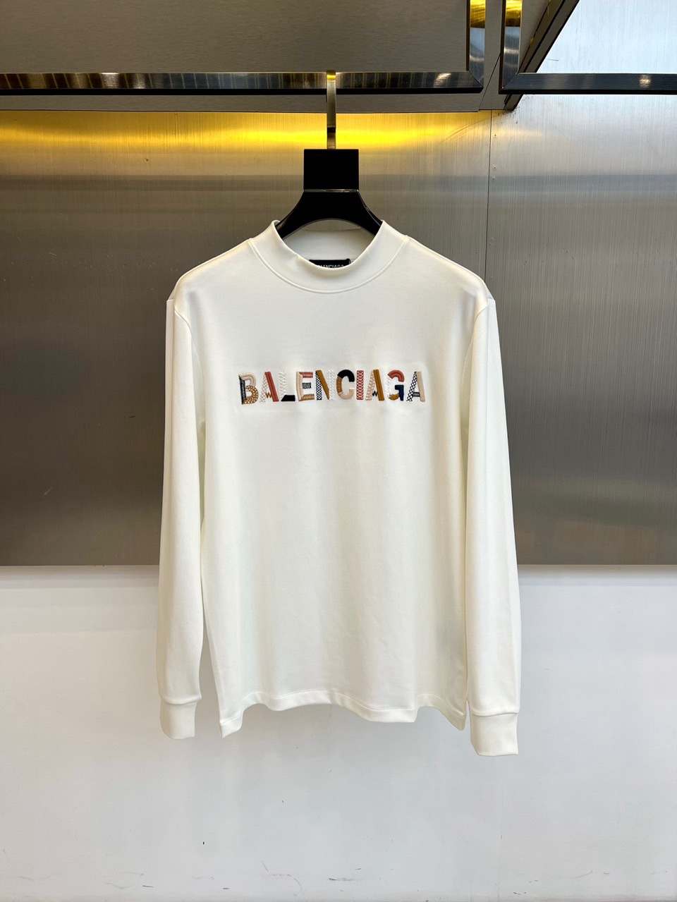 NO:621892,Ba Balenciaga's new autumn and winter modal long-sleeved top outlines a simple and modern silhouette through a half-high collar design. The body is made of high-quality modal fabric, showing a velvety soft and skin-friendly texture, with excellent drape and breathability. The biggest highlight is the eye-catching chest  Brand logo design - using hot stamping technology combined with brown three-dimensional letters to spell out the word 'BALENCIAGA', in which the letter 'E' is cleverly integrated into the iconic double B totem, paired with dark blue strokes on the edge, forming a rich visual hierarchy. Modification  The body cut and half-high neckline perfectly balance the need for warmth and fashion. Whether worn alone with jeans to show a minimalist style, or worn as an inner layer with a suit or leather jacket, it can highlight Balenciaga's iconic deconstructed aesthetics. This piece combines comfortable wearing experience with  The combination of avant-garde design language has become an indispensable and versatile tool in the autumn and winter wardrobe. 48-56 (model weighs 173,143 pounds, upper body size 50),,balenciaga,balenciaga,jeans,leather  jacket,business suit,alexander wang19860909Ba巴黎世家、秋冬新品莫代尔长袖上衣,通过半高领设计勾勒出简约摩登的轮廓.衣身采用高品质莫代尔面料,呈现丝绒般柔软亲肤的质感,兼具优良垂坠感与透气性.最大亮点在于胸前醒目的品牌标识设计——以烫金工艺结合棕色调立体字母拼出'BALENCIAGA'字样,其中字母'E'巧妙融入了标志性的双B图腾,搭配边缘的深蓝色描边处理,形成丰富的视觉层次.修身剪裁与半高领口完美平衡了保暖需求与时尚感,无论是单独搭配牛仔裤展现极简风格,还是作为内搭与西装或皮衣叠穿,都能突显巴黎世家标志性的解构主义美学.这件单品将舒适穿着体验与前卫设计语言相结合,成为秋冬衣橱中不可或缺的百搭利器.48-56（模特173,143斤上身50码）,,balenciaga,balenciaga,jeans,leather jacket,business suit,alexander wang,Men's clothing