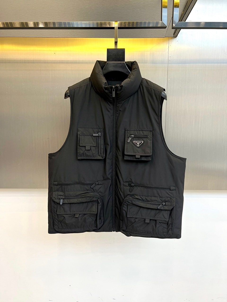 NO:626374,Prad's new men's down vest for autumn and winter uses deep black to interpret modern functional aesthetics. The stand-up collar design and smooth zipper opening create a neat silhouette. The multi-level pocket layout on the front shows exquisite craftsmanship. It is equipped with small zippered pockets on both sides. The middle is decorated with the brand's classic triangular logo decorative bag, and there is a large-capacity zipper pocket below, which perfectly combines practical functions and decorative beauty.  The vest is made of crisp material with simple and powerful lines. The filling contains 90% high-quality down to ensure lightness and warmth. The details highlight the luxurious quality. For example, the label indicates that the clothing contains non-textile parts of animal origin (such as fine leather decoration). It is recommended that professional care be used to dry clean. A pad should be used to protect the leather part when ironing. Do not wash or bleach.  The unique charm of this vest lies in the perfect combination of practical functionality and Italian elegance. The multi-pocket design not only meets daily storage needs, but also builds a rich visual hierarchy. Whether it is paired with a shirt to create a business casual look, or layered inside a jacket to enhance the sense of layering, it can show a modern urban look.  Men's exquisite taste. Prada redefines the luxurious dimension of functional items through this design, injecting modern choices that are both practical and aesthetic into the autumn and winter wardrobe. 48-56 (model 173, 143 pounds, upper body size 50),, prada, prada, jackets  & coats,shirts,down jacket,alexander wang19860909Prad普拉、秋冬新品男士羽绒马甲,以深邃黑色演绎现代机能美学.立领设计与顺滑拉链开合营造出利落轮廓,正面多层次口袋布局展现精湛工艺上方两侧配备带拉链小口袋,中部点缀品牌经典三角形徽标装饰袋,下方则设大容量拉链口袋,完美融合实用功能与装饰美感. 马甲采用挺括材质制作,线条简洁有力.填充物含90优质羽绒,确保轻盈保暖性.细节处彰显奢华品质,如标签提示衣物含有动物源非纺织部件（如精致皮革装饰）,建议专业护理需采用干洗方式,熨烫时需垫布保护皮革部分,不可水洗漂白. 这款马甲的独特魅力在于将实用机能风与意式优雅完美结合.多口袋设计既满足日常收纳需求,又构建出丰富的视觉层次.无论是搭配衬衫打造商务休闲造型,还是叠加在外套内增强穿搭层次感,都能展现出现代都市男士的精致品味.普拉达通过这款设计重新定义了功能性单品的奢华维度,为秋冬衣橱注入兼具实用与美学的摩登选择.48-56（模特173,143斤上身50码）,,prada,prada,jackets & coats,shirts,down jacket,alexander wang,Men's clothing