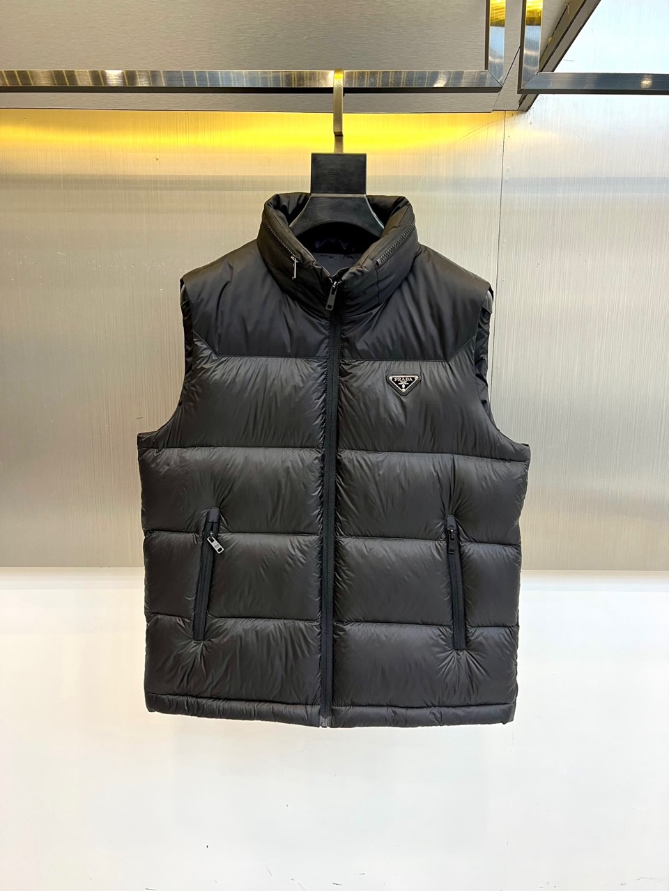 NO:626380,Prada's new autumn and winter black down vest interprets modern luxury with a simple design. The stand-up collar shape is matched with smooth zipper opening and closing, which outlines clean lines. The brand's iconic triangular metal logo is embellished on the chest, becoming the overall visual focus. The zipper pockets on both sides not only meet practical needs, but also add a level of detail to the simple design.  This vest uses a unique fabric combination. The exterior and lining are made of cotton, which is stiff and comfortable; the filling is a high-quality blend of 90 white goose down and down, ensuring light and warm performance. The carefully designed quilting process allows the vest to maintain fluffiness without looking bloated, perfectly balancing temperature and style.  Details highlight the brand's insistence on quality. The label indicates that the product contains non-textile parts of animal origin, and professional care is recommended. Special attention must be paid to protecting the leather decoration when dry cleaning, and a cloth is required for ironing. These meticulous care requirements reflect the high-end positioning of the single product.  Its style wanders between formal and casual, and can be paired with a shirt to create a business casual look, or combined with a sweater to present an urban casual style. Prada demonstrates its precise grasp of the balance between functionality and aesthetics through this vest, providing a practical and fashionable exquisite item for autumn and winter layering. 48-56 (model 173,143 pounds, upper body size 50),, prada, prada, shirts, down jacket, alexander wang19860909Prad普拉达、秋冬新品黑色羽绒马甲以简约设计诠释现代奢华.立领造型搭配顺滑拉链开合,勾勒出利落线条.胸前点缀品牌标志性三角形金属徽标,成为整体的视觉焦点.两侧的拉链口袋既满足实用需求,又为简约设计增添细节层次. 这款马甲采用独特的面料组合外部与衬里使用棉质材质,挺括舒适；填充物为90白鹅绒与羽绒的优质混合,确保轻盈保暖的性能.精心设计的绗缝工艺使马甲保持蓬松度而不显臃肿,完美平衡温度与风度. 细节处彰显品牌对品质的坚持标签提示产品含有动物源非纺织部件,建议专业护理.干洗时需特别注意保护皮革装饰,熨烫需垫布操作,这些细致的护理要求正体现了单品的高端定位. 其风格游走于正式与休闲之间,可搭配衬衫打造商务休闲造型,亦可与针织衫组合呈现都市休闲风范.普拉达通过这款马甲展现了其对功能性与美学平衡的精准把握,为秋冬叠穿提供了一件兼具实用与时尚的精致单品.48-56（模特173,143斤上身50码）,,prada,prada,shirts,down jacket,alexander wang,Men's clothing
