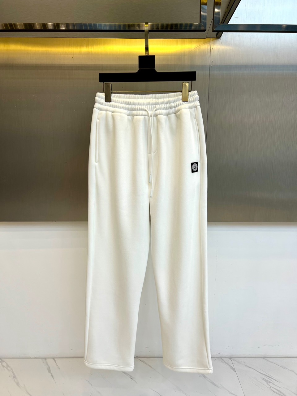 NO:626394,Stone Island's new autumn and winter velvet trousers feature a double adjustment system of elastic bands and drawstrings at the waist to achieve a personalized fit experience. The straight-cut trouser leg design creates smooth lines and is tolerant to all body shapes. The iconic black square brand logo on the left trouser leg becomes the finishing touch, low-key highlighting the brand identity.  The ribbed cuff design at the trouser legs reflects exquisite craftsmanship, and the fine stitching ensures firmness and durability. The velvet lining is made of high-quality velvet material, which maintains the outer crisp shape while providing a warm and comfortable wearing experience. The surface of the fabric has a fine velvet texture, which not only retains the skin-friendly properties of cotton materials, but also has good thermal insulation properties.  These trousers perfectly balance function and fashion. The white main color has both refreshing feeling and matching potential. Its simple design can be easily integrated into a variety of dressing styles. Whether it is paired with a down jacket to create an urban outdoor look, or combined with a sports top for a casual style, it can show outstanding taste.  Stone Island combines practical details with modern tailoring to create this versatile item suitable for daily commuting, weekend leisure and other scenarios, injecting a high-quality choice that is both practical and fashionable into the autumn and winter wardrobe. S-XXL (please state your height and weight when placing an order),,down  jacket,alexander wang19860909Stone Island石头岛、秋冬新品加绒长裤,腰部采用松紧带与抽绳双重调节系统,实现个性化贴合体验.直筒剪裁的裤腿设计营造流畅线条,对各类身形展现包容性.左侧裤腿处的标志性黑色方形品牌徽标成为点睛之笔,低调彰显品牌身份. 裤脚处的罗纹收口设计体现精湛工艺,细密缝线确保牢固耐用.加绒内里选用高品质绒料,在保持外部挺括造型的同时提供温暖舒适的穿着体验.面料表面呈现细腻绒毛质感,既保留棉质材料的亲肤特性,又具备良好的保暖性能. 这款长裤完美平衡功能与时尚,白色主调兼具清爽感与搭配潜力.其简约设计能轻松融入多种穿搭风格,无论是搭配羽绒服打造都市户外造型,还是结合运动上衣展现休闲风尚,都能展现出众的品味.石头岛通过将实用细节与现代剪裁相结合,创造出这款适合日常通勤、周末休闲等多场景的百搭单品,为秋冬衣橱注入兼具实穿性与时尚感的优质选择.S-XXL（下单请报身高体重）,,down jacket,alexander wang,Men's clothing