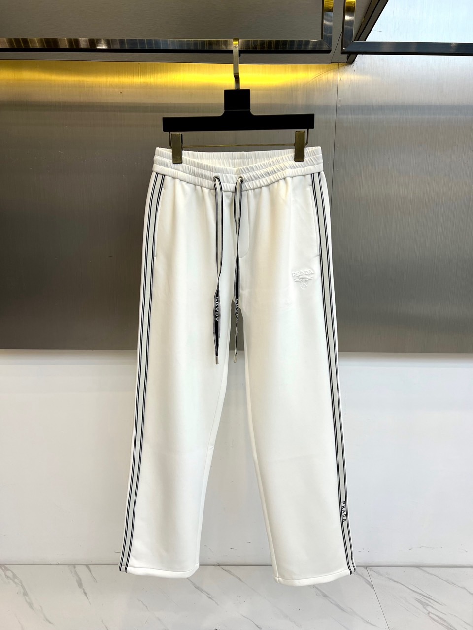 NO:626410,Prada's new autumn and winter velvet trousers feature an elasticated waistband with black drawstrings for a comfortable fit. The black stripes on both sides of the trouser legs form a visual extension with the brand logo, subtly elongating the leg lines. The front of the trousers is embellished with exquisite brand embroidery, low-key highlighting a luxurious identity.  The fabric is made of high-quality velvet material, with fine and soft velvet on the inside and a crisp silhouette on the outside. The side stripes not only strengthen the brand recognition, but also give the item a sporty and fashionable feel. The straight cut takes into account both wearing comfort and neat silhouette, and the simple black and white contrasting color scheme shows eternal elegance.  These fleece pants perfectly balance practicality and fashion. They can be paired with sneakers to create an urban casual look, or combined with a coat for a mixed style. Through precise control of details, Prada integrates sports elements into high-end fashion, injecting essential items with both comfort and sophistication into the autumn and winter wardrobe. 48-56 (model 173, 143 pounds, upper body size 50),, prada, prada, sneakers, alexander wang19860909Prad普拉达、秋冬新品加绒裤,松紧腰头搭配黑色抽绳实现舒适贴合,裤腿两侧的黑色条纹与品牌标识形成视觉延伸,巧妙拉长腿部线条.裤身正面点缀精致品牌刺绣,低调彰显奢华身份. 面料选用高品质加绒材质,内部绒面细腻柔软,外部保持挺括版型.侧边条纹不仅强化品牌辨识度,更赋予单品运动时尚感.直筒剪裁兼顾穿着舒适度与利落轮廓,黑白对比的简洁配色展现永恒优雅. 这款加绒裤完美平衡实用性与时尚感,既能搭配运动鞋打造都市休闲造型,亦可与大衣组合呈现混搭风格.普拉达通过精准的细节把控,将运动元素融入高端时尚,为秋冬衣橱注入兼具舒适度与精致感的必备单品.48-56（模特173,143斤上身50码）,,prada,prada,sneakers,alexander wang,Men's clothing