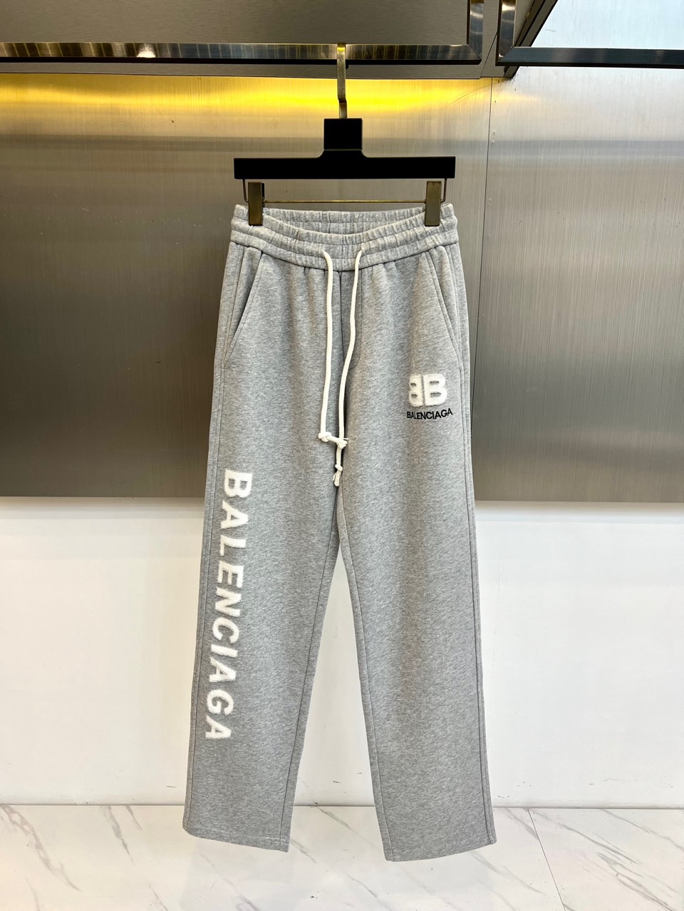 NO:626418,Ba Balenciaga, autumn and winter velvet pants, present the iconic street aesthetic in light gray. The elastic waistband and drawstring design ensure wearing comfort. The eye-catching BALENCIAGA words on the side of the trouser legs and the BB logo on the knees form a layered print. The velvet lining provides a warm experience in autumn and winter, and the straight cut fits the brand. Oversize  Style. This single product transforms the brand logo into visual language, suitable for matching with sports shoes to create an urban casual look, interpreting Balenciaga's iconic trend attitude and practicality. 48-56 (model 173, 143 pounds, upper body size 50),, balenciaga, balenciaga, versace, sneakers, alexander wang19860909Ba巴黎世家、秋冬加绒裤,以浅灰色呈现标志性街头美学.松紧腰头搭配抽绳设计确保穿着舒适度,裤腿侧面醒目的BALENCIAGA字样与膝盖处的BB标志形成层次感印花.加绒内里提供秋冬保暖体验,直筒剪裁契合品牌 Oversize 风格.这款单品将品牌标识转化为视觉语言,适合搭配运动鞋打造都市休闲造型,诠释了巴黎世家标志性的潮流态度与实穿主义.48-56（模特173,143斤上身50码）,,balenciaga,balenciaga,versace,sneakers,alexander wang,Men's clothing