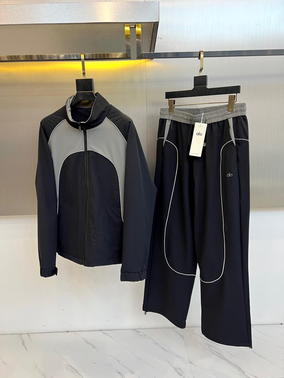 NO:648449,Alo  The autumn and winter series reshape the sports and leisure style with forward-looking design language. This sports suit includes a stand-up collar zipper jacket and a pair of wide-leg sports trousers. The jacket uses high-end black and gray two-color splicing, with neat and smooth lines, and the stand-up collar design and front center zipper are taken into account  It has a sense of protection and modern style. The trousers are based on pure black, with a contrasting gray elastic waistband. The white double stripes extending from the side to the trouser legs are the finishing touch, which visually greatly lengthens the leg lines. The suit uses the brand's iconic high-performance  The fabric ensures freedom of stretch during exercise and comfortable drape for daily wear. It cleverly combines the functional core of professional sportswear with the wide aesthetics of street fashion. The simple color scheme of black and white and gray is advanced and versatile. Whether it is used for high-intensity training or as a fashionable style for daily travel, it can be easily controlled, perfectly interpreting the modern lifestyle advocated by Alo that is both energetic and stylish. 48-56 (model 173, 143 pounds, upper body size 50),,jackets  & coats,alexander wang19860909Alo 秋冬系列以前瞻性设计语言重塑运动休闲风尚.本款运动套装包含一件立领拉链夹克与一条阔腿运动长裤.夹克采用高级黑灰双色拼接,线条利落流畅,立领设计与前中拉链兼顾防护感与摩登型格.长裤则以纯黑为基调,搭配对比鲜明的灰色弹力腰头,侧边延伸至裤脚的白色双条纹成为点睛之笔,在视觉上极大拉长腿部线条.套装选用品牌标志性的高性能面料,确保运动时的伸展自由与日常穿着的舒适垂坠.它将专业运动服饰的功能内核与街头潮流的阔型美学巧妙融合,黑白灰的简约配色高级且百搭.无论是用于高强度训练,还是作为日常出行的时尚造型,都能轻松驾驭,完美诠释了Alo所倡导的、兼具活力与型格的现代生活方式.48-56（模特173,143斤上身50码）,,jackets & coats,alexander wang,Men's clothing
