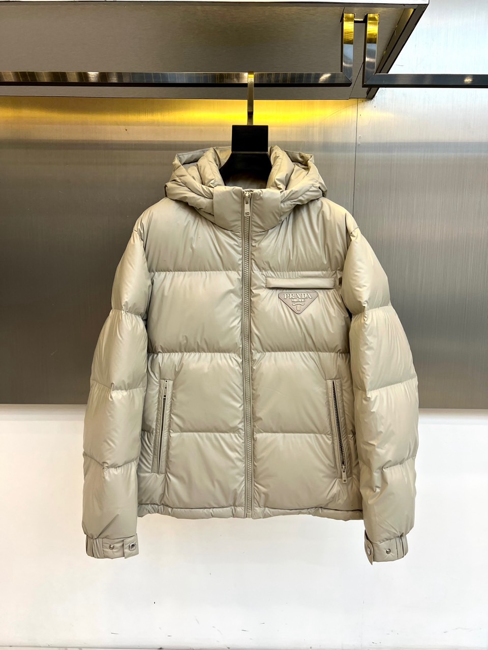 NO:653687,Prada, the new goose down jacket for autumn and winter, adopts a hooded design with an adjustable brim to enhance practical protection. The body lines are smooth and neat, and the uniform quilting process ensures that the filling is full and fixed. The iconic triangular metal logo is embellished on the front to highlight the brand identity. Zippered diagonal pockets are equipped on both sides, taking into account storage safety and visual simplicity. The cuffs are designed with windproof tightening, and exquisite craftsmanship is reflected in the details.  The fabric is made of polyurethane composite polyester fiber base fabric, which gives the clothes good texture and stiffness; the lining is nylon, which is smooth to the touch. The core filling is high-quality goose down, with a velvet content of up to 90%, which is light and fluffy and has excellent temperature locking performance. The brim and other parts are filled with polyester fiber to ensure the shape while optimizing local warmth.  Combining Italian precision workmanship with functional aesthetics, metal logos and sharp tailoring become a low-key luxury statement. This goose down jacket can be paired with formal wear to create a modern urban image, or it can be integrated into casual daily wear, perfectly interpreting Prada's design philosophy of combining pragmatism and high fashion. 48-56 (model 173, 143 pounds, upper body size 50),, prada, prada, hats, alexander wang19860909Prad普拉达、秋冬新品鹅绒服,款式采用连帽设计,帽檐可调节,增强实用防护性.衣身线条流畅利落,均匀的绗缝工艺确保填充物饱满且定型.正面点缀标志性的三角形金属徽标,彰显品牌身份.两侧配备带拉链的斜插口袋,兼顾储物安全与视觉简洁.袖口设有防风收紧设计,细节处体现精湛工艺. 面料采用聚氨酯复合聚酯纤维底布,赋予衣物良好的质感与挺括度；里料为锦纶,触感顺滑.核心填充物为高品质鹅绒,绒子含量高达90,轻盈蓬松,锁温性能卓越.帽檐等部位采用聚酯纤维填充,保障造型的同时优化局部保暖. 将意式精工与机能美学相融合,金属徽标与利落剪裁成为低调的奢华宣言.这款鹅绒服既能搭配正装塑造摩登都市形象,亦可融入休闲日常穿搭,完美诠释普拉达融合实用主义与高级时装的设计哲学.48-56（模特173,143斤上身50码）,,prada,prada,hats,alexander wang,Men's clothing