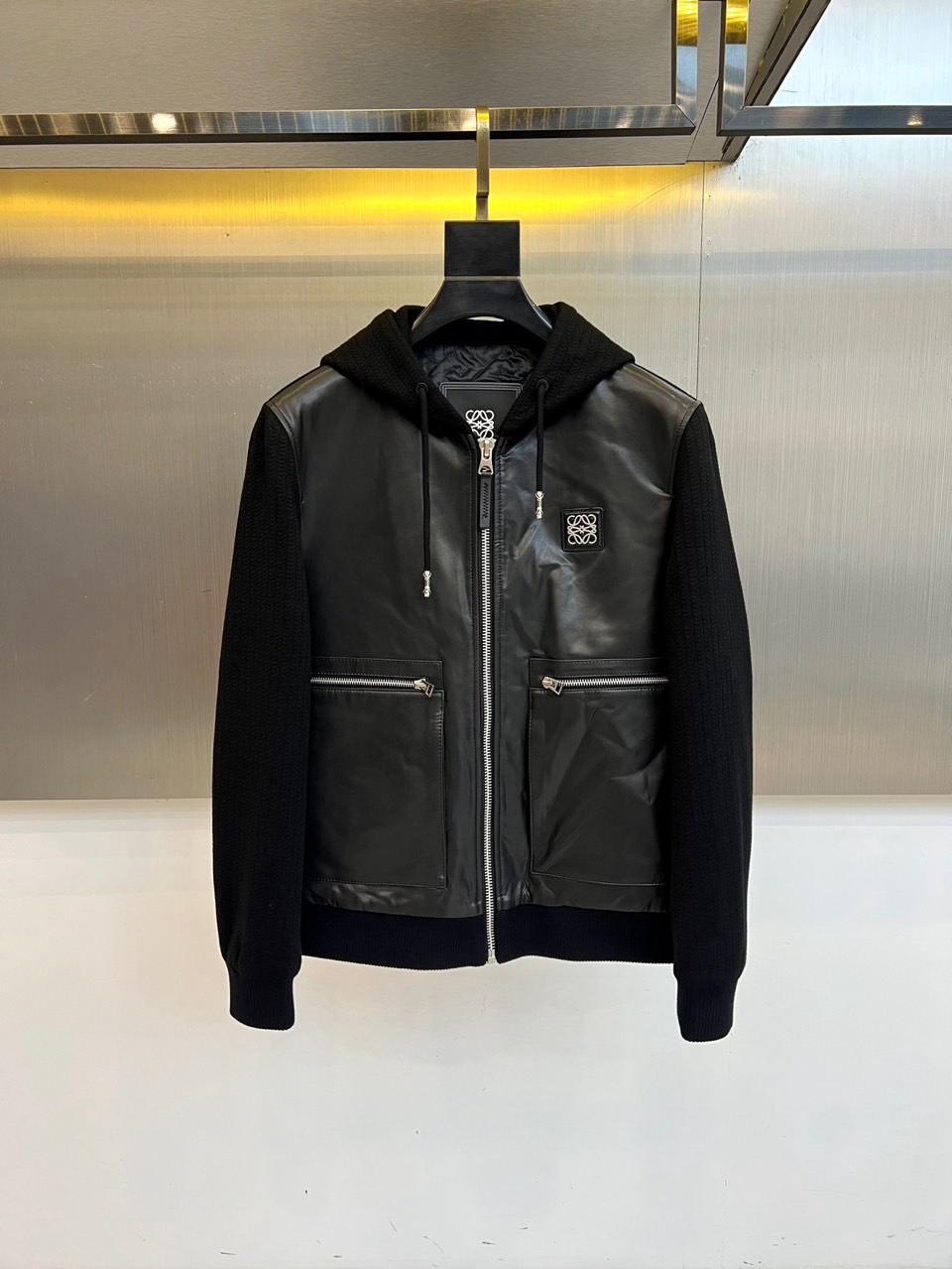 NO:648437,Loewe, autumn and winter series hooded leather jacket. Large body sheepskin. The core of this black hooded jacket lies in the ingenious splicing of high-grade sheepskin and knitted sleeves. The tough texture of the glossy leather is in sharp contrast with the soft knitted texture. It is a combination of strength and softness, breaking the rules. The front chest is decorated with the brand's iconic silver Anagram pattern metal logo, which is low-key and eye-catching. The silver zipper running through the skirt and the symmetrical oblique zipper pocket have both smooth visual and practical functions. Adjustable  The drawstring hooded design injects casual dynamics into the overall silhouette. It seamlessly combines exquisite leather craftsmanship with comfortable sports and leisure silhouettes, finding the perfect balance between the free and easy street style and the sophistication of high fashion. It is not only a cold-proof item, but also a style statement that highlights unique personality and extraordinary taste, easily managing diverse scenes from daily travel to fashion gatherings. 48-56 (model 173, 143 pounds, upper body size 50),, loewe, jackets  & coats,sheepskin,hats,alexander wang19860909Lowo罗意威、秋冬系列连帽皮夹克.大身绵羊皮.本款黑色连帽夹克,核心在于高级绵羊皮与针织袖的匠心拼接,光泽皮革的硬朗质感与柔软针织的纹理形成鲜明对比,刚柔并济,突破常规.前胸饰以品牌标志性的银色Anagram图案金属徽标,低调而瞩目.贯穿衣襟的银色拉链与对称的斜插拉链口袋,兼具流畅视觉与实用功能.可调节抽绳连帽设计,为整体廓形注入随性动感.它将精湛的皮革工艺与舒适的运动休闲轮廓无缝结合,在街头感的洒脱与高级时装的精致之间找到完美平衡,不仅是一件御寒单品,更是彰显独特个性与不凡品味的风格宣言,轻松驾驭从日常出行到时尚聚会的多元场景.48-56（模特173,143斤上身50码）,,loewe,jackets & coats,sheepskin,hats,alexander wang,Men's clothing