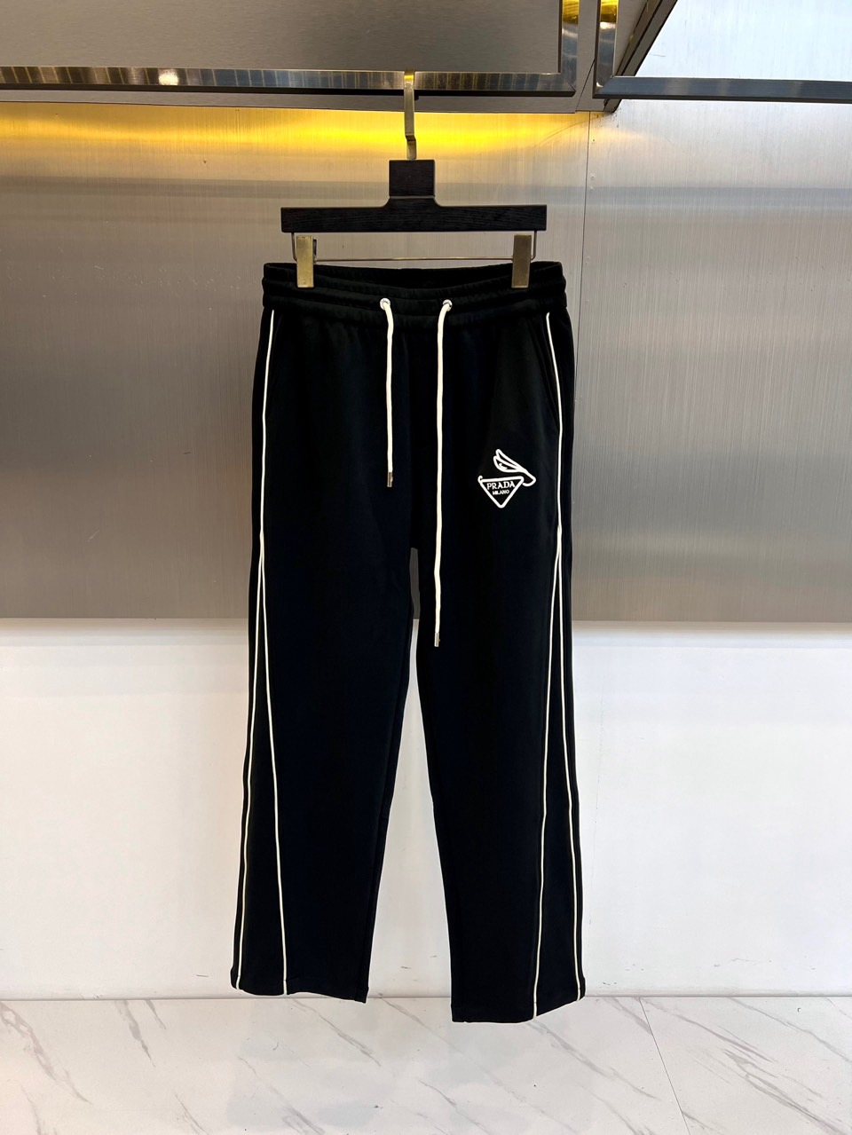 NO:650792,Prad, the new black casual sweatpants for autumn and winter 2025, interprets modern casual aesthetics with a classic straight fit. These sweatpants are made of high-quality fabrics, and the waistband is equipped with an adjustable drawstring design to ensure wearing comfort and can adapt to different waist needs. Eye-catching white lines are decorated on both sides of the pants, adding a visual layer and dynamic atmosphere to the overall design. The exquisite Prada brand logo and wing pattern are printed on the left side, low-key highlighting the brand genes.  Its design perfectly combines simplicity and trendy elements. The straight cut takes into account both freedom of movement and clean silhouette. The clever use of white lines breaks the pure black tone and injects fashionable vitality. In terms of style, these sweatpants are suitable for a variety of occasions. Whether it is paired with a simple sweater to create a daily casual look, or paired with a sports jacket to show a dynamic style, it can easily enhance the overall look.  .From going out in the city to light sports, it can use Prada's consistent exquisite craftsmanship and low-key luxury, becoming a must-have item in the autumn and winter wardrobe that is both practical and fashionable. 48-56 (model weighs 173,143 pounds, upper body size 50),, prada, prada, hoodie, sweatshirts, jackets  & coats,alexander wang19860909Prad普拉达、2025秋冬新品黑色休闲卫裤以经典直筒版型演绎现代休闲美学.这款卫裤采用高品质面料制作,裤腰配备可调节抽绳设计,确保穿着舒适度并能适应不同腰围需求.裤身两侧饰以醒目的白色线条,为整体设计增添视觉层次与动感气息,左侧印有精致的Prada品牌标识及翅膀图案,低调彰显品牌基因. 其设计将简约与潮流元素完美融合,直筒剪裁兼顾活动自由度与利落轮廓,白色线条的巧妙运用打破纯黑基调,注入时尚活力.风格上,这款卫裤适合多种场合,无论是搭配简约卫衣打造日常休闲造型,还是配合运动外套展现活力风范,都能轻松提升整体穿搭质感.从城市出街到轻度运动,它都能以普拉达一贯的精湛工艺与低调奢华,成为秋冬衣橱中兼具实穿性与时尚感的必备单品.48-56（模特173,143斤上身50码）,,prada,prada,hoodie,sweatshirts,jackets & coats,alexander wang,Men's clothing