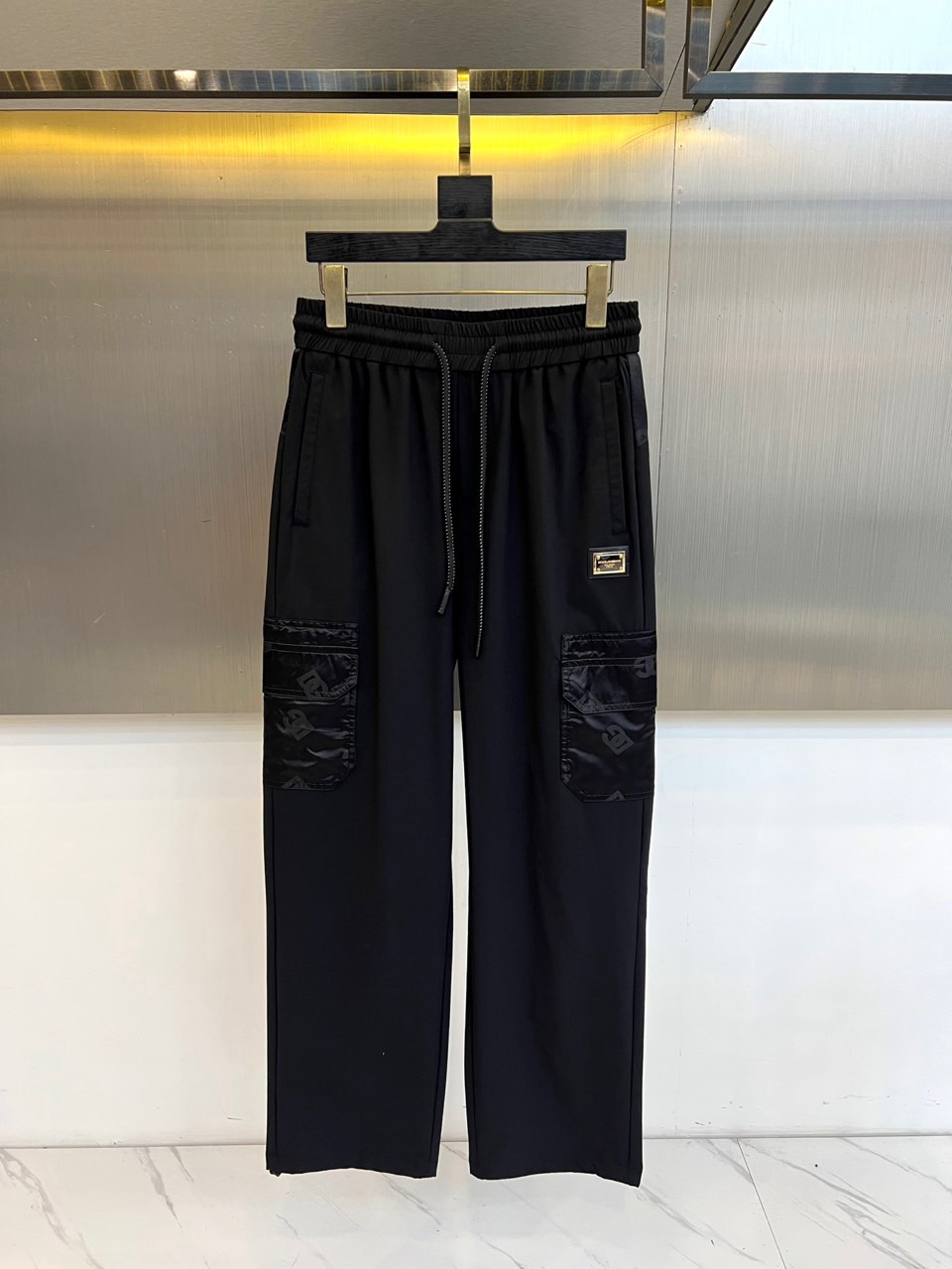 NO:650760,DG Dolce & Gabbana, 2025 autumn and winter, reshapes daily casual aesthetics with exquisite prints. This black trousers uses an elastic drawstring elastic waistband to ensure all-day comfort. Its iconic design is the three-dimensional large pockets on both sides, decorated with unique exquisite dark pattern printing, showing ingenuity in the details. The classic metal logo above the right pocket low-key confirms the brand's luxury gene. Smooth tailoring and drape surface  It combines materials and maintains neat lines in a loose silhouette. It integrates the essence of Italian luxury into functional streetwear, and uses classic black to achieve versatile attributes. Whether it is a casual trip or a city stroll, it can easily show an eclectic and modern style. 48-56 (model 173, 143 pounds, upper body size 50), Dolce&Gabbana, alexander  wang19860909DG杜嘉班纳、2025秋冬,以精致印花重塑日常休闲美学.本款黑色长裤采用弹力抽绳松紧腰头,确保全天候舒适自如.其标志性设计在于两侧立体大口袋,饰有独特的精致暗纹印花,细节处彰显匠心.右袋上方的经典金属标识,低调印证品牌奢华基因.流畅的剪裁与垂坠面料结合,在宽松廓形中保持利落线条.它将意式奢华精髓融入街头功能装束,以经典的黑色成就百搭属性,无论是休闲出行或都市漫步,皆能轻松展现不拘一格的摩登型格.48-56（模特173,143斤上身50码）,,Dolce&Gabbana,alexander wang,Men's clothing