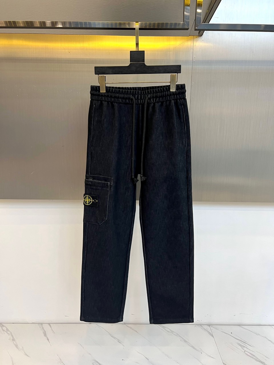 NO:650766,STONE ISLAND, new product for autumn and winter 2025, Compass Badge Elastic Waist Casual Pants are made of classic dark blue washed denim fabric to reshape contemporary functional aesthetics. These jeans are designed with a fully elastic waistband and a built-in drawstring of the same color to achieve one-click putting on and taking off and precise fit. There is a three-dimensional functional pocket on the left thigh, with the brand's iconic compass badge sewn on the bag surface, and the direction scale and 'STONE' are engraved with exquisite embroidery technology.  ISLAND' has become the visual focus and identity imprint of the entire item. The slim straight cut is neat and smooth, adapting to a variety of body shapes. The fabric has been specially washed to present a delicate vintage texture and a comfortable wearing texture. The combination of elastic waistband and three-dimensional pockets integrates the brand's consistently explored functional concepts into daily design, which not only meets the convenience needs of urban life, but also retains a distinct nautical adventure gene. This pair of jeans is a versatile item that connects work, leisure and outdoor scenes, perfectly interpreting Stone Island  Continuous deconstruction and re-creation of materials, functions and symbols. 48-56 (model weighs 173,143 pounds, upper body size 50),,versace,jeans,alexander wang19860909STONE ISLAND 石头岛、2025秋冬新品 罗盘徽章松紧腰休闲裤 以经典深蓝水洗牛仔面料,重塑当代机能美学.这款牛仔裤采用全松紧腰头设计,内置同色系抽绳,实现一键穿脱与精准贴合.左侧大腿处搭载立体功能口袋,袋面缝制品牌标志性罗盘徽章,以精湛刺绣工艺镌刻方向刻度与“STONE ISLAND”字样,成为整件单品的视觉焦点与身份印记.修身直筒剪裁利落流畅,适应多种身形. 面料经过特殊水洗处理,呈现细腻复古肌理与舒适穿着质感.松紧腰头与立体口袋的搭配,将品牌一贯探索的机能理念融入日常设计,既满足了都市生活对便捷的需求,亦保留了鲜明的航海探险基因.这条牛仔裤是连接工作、休闲与户外场景的 versatile 单品,完美诠释 Stone Island 对材质、功能与符号的持续解构与再创造.48-56（模特173,143斤上身50码）,,versace,jeans,alexander wang,Men's clothing