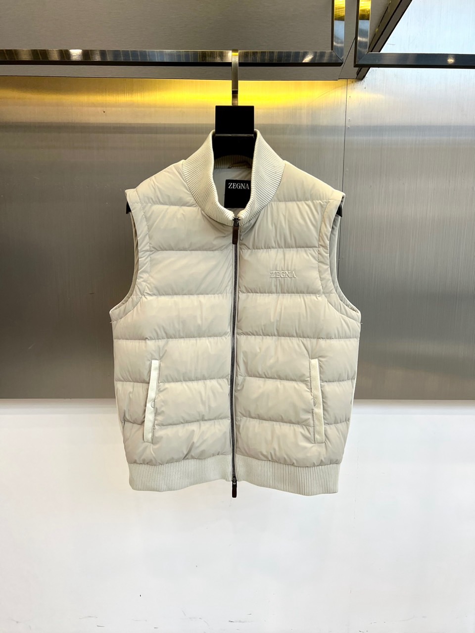 NO:726330,after the year  Zegna Zegna's new autumn and winter down vest, with light beige as the main color, shows the elegance of a modern gentleman through its stand-up collar design and precise tailoring. This vest is filled with high-quality down and has a regular quilted plaid pattern on the surface, which is effective in fixing  Thermal insulation material adds a three-dimensional texture. The front placket is equipped with a smooth zipper opening and closing system, and the pockets on both sides are decorated with white piping details, which cleverly echoes the overall simple style. The collar and hem are made of elastic rib knitting technology to ensure a comfortable fit and not easy to deform. Left  The brand logo is embellished on the chest, showing off the luxury genes in a low-key manner. The fabric is made of polyamide, which has both light texture and durability. The lining contains 91 polyamide and 9 elastic fibers, which provide moderate extensibility. As a layering tool in autumn and winter, it can be paired with shirts or sweaters to create a multi-layered look, perfectly balancing practical functions and Italian aesthetics. It is suitable for business, leisure and daily social occasions. 48-56 (model 173, 143 pounds, upper body size 50),,zegna,shirts,down  jacket,19860909年后 Zegna杰尼亚、秋冬新品羽绒马甲,以浅米色为主色调,通过立领设计与精准剪裁展现现代绅士的优雅风度.这款马甲采用高品质羽绒填充,表面呈现规整的绗缝格纹,既有效固定保暖材料又增添立体质感.前襟配备顺滑拉链开合系统,两侧口袋饰以白色滚边细节,与整体简约风格形成巧妙呼应.衣领及下摆采用弹性罗纹针织工艺,确保贴合舒适且不易变形.左胸处点缀品牌标识,低调彰显奢华基因.面料选用聚酰胺材质,兼具轻盈质感与耐用特性,里料含91聚酰胺与9弹性纤维,提供适度延展性.作为秋冬叠穿利器,可搭配衬衫或针织衫打造多层次造型,完美平衡实用功能与意式美学,适用于商务休闲与日常社交等多种场合.48-56（模特173,143斤上身50码）,,zegna,shirts,down jacket,,Men's clothing