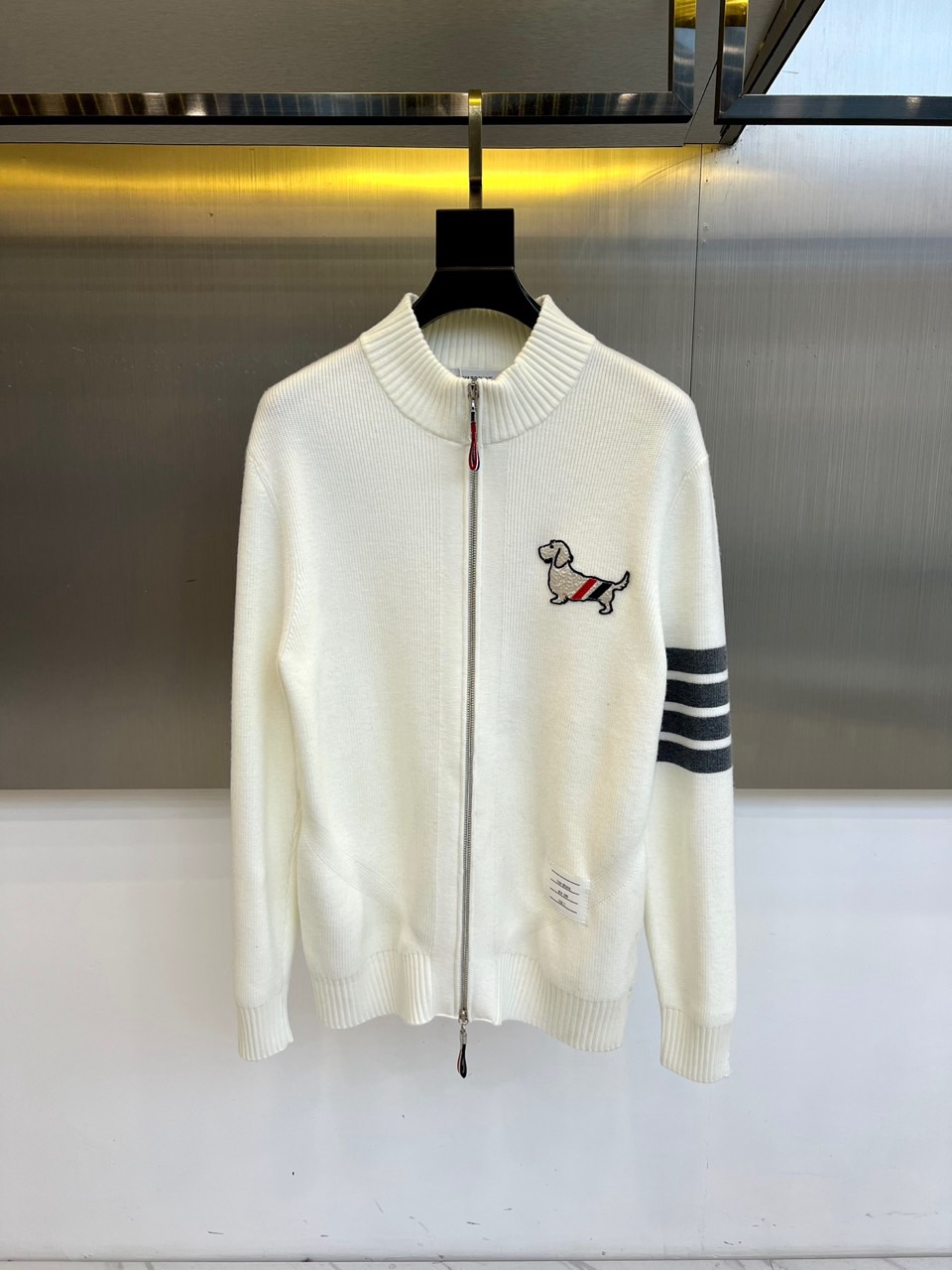 NO:656067,: THOM BROWNE  Tom Brown, the new white knitted cardigan for autumn and winter 2025, reinvents the classic with the iconic design language. The stand-up collar and zipper closure are both neat and convenient. The left chest is decorated with interesting puppy embroidery, decorated with red, white and blue brand stripes; the left sleeve is decorated with classic black, white and gray stripes, cleverly echoing the brand genes. The hem and cuffs are closed with comfortable ribs. Fine  The 98% cotton fabric is selected and manufactured in Japan to ensure a soft and skin-friendly wearing experience. The overall style combines rigorous academic style with playful details. Whether it is paired with a shirt or simple inner wear, it can easily enhance the style and become an indispensable fashionable item in the autumn and winter wardrobe. 48-56 (model is 173, 143 pounds, upper body size 50),,thom  browne,shirts,alexander wang19860909: THOM BROWNE 汤姆布朗、2025秋冬新品白色针织开衫,以标志性设计语言重塑经典.立领与拉链开合,兼具利落感与便捷.左胸点缀趣味小狗刺绣,缀以红、白、蓝品牌条纹；左袖饰有经典黑、白、灰三色条纹,巧妙呼应品牌基因.下摆与袖口采用舒适罗纹收口.精选98棉质面料,于日本精工制造,确保柔软亲肤的穿着体验.整体将严谨的学院风与玩味细节融合,无论是搭配衬衫或简约内搭,皆能轻松提升造型层次,成为秋冬衣橱中不可或缺的时髦单品.48-56（模特173,143斤上身50码）,,thom browne,shirts,alexander wang,Men's clothing