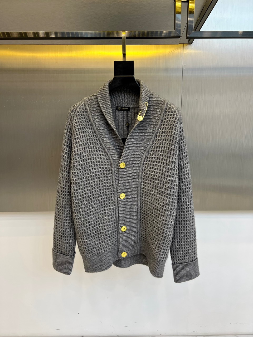 NO:656073,Vers Versace, the new 2025 autumn and winter knitted cardigan, uses high-end gray tones and unique grid texture to reshape the classic gentleman's wardrobe. The green fruit collar design has smooth lines, and a silver pin decoration on the collar instantly lights up the details, highlighting the Italian luxury gene. The eye-catching yellow buttons contrast sharply with the gray body, becoming the finishing touch of the whole. The long sleeves are matched with ribs  The neckline is neat and stylish. The overall comfort of classic knitting is cleverly combined with Versace's iconic gorgeous aesthetics. Whether it is daily layering or formal occasions, it can easily show a calm and extraordinary fashion aura. 48-56 (model 173, 143 pounds, upper body size 50),,versace,versace,alexander  wang19860909Vers范思哲、2025秋冬新品针织开衫,以高级灰色调与独特网格纹理,重塑经典绅士衣橱.青果领设计线条流畅,领口一枚银色别针装饰,瞬间点亮细节,彰显意式奢华基因.醒目的黄色纽扣与灰色主体形成鲜明对比,成为整体点睛之笔.长袖搭配罗纹收口,利落有型.整体将经典针织的舒适感与范思哲标志性的华丽美学巧妙融合,无论是日常叠穿还是正式场合,皆能轻松展现从容不凡的时尚气场.48-56（模特173,143斤上身50码）,,versace,versace,alexander wang,Men's clothing