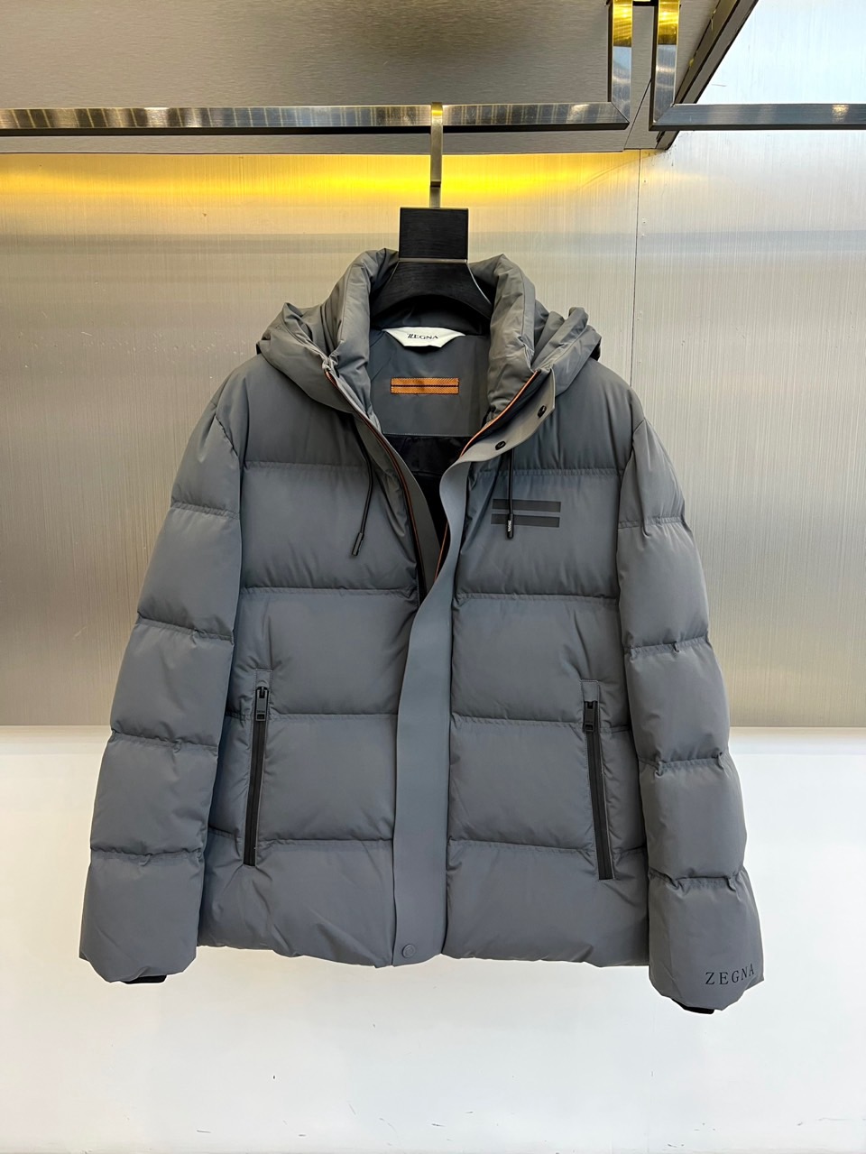 NO:656093,Zegn Ermenegildo Zegna's 2025 autumn and winter new down jacket interprets modern urban outdoor aesthetics with calm tones. The style adopts a hooded design, and the hood is equipped with an adjustable drawstring and a button windshield to enhance practical protection. The front is divided by horizontal quilting, taking into account the bulkiness and clean outline. The left chest is decorated with two dark stripes, and the lower side of the right sleeve is embellished with the brand logo. Both sides are equipped with zippered slant pockets for safe storage and smooth lines.  The fabric is made of high-density polyester fiber, which is windproof and waterproof, and is filled with high-quality down to ensure warmth and lightness. The details reflect Italian precision, such as the smooth zipper system and uniform quilting. The overall design combines Alpine functional genes with urban simplicity, and the horizontal quilting and armbands become low-key identity marks.  This down jacket can not only cope with urban autumn and winter commuting, but also accompany outdoor trips on weekends. It perfectly interprets Zegna's design philosophy of integrating high-performance materials and Italian elegance. The product is marked as produced in China and strictly follows the brand's process standards to achieve seamless switching from mountain-inspired urban scenes. 48-56 (model 173, 143 pounds, upper body size 50),,zegna,down jacket,hats,alexander wang19860909Zegn杰尼亚、2025秋冬新品羽绒服,以沉稳色调诠释现代都市户外美学.款式采用连帽设计,帽部配备可调节抽绳与纽扣挡风片,增强实用防护性.正面运用横向绗缝分割,兼顾蓬松度与利落轮廓.左胸饰有两道深色条纹装饰,右袖下侧点缀品牌标识.两侧配备带拉链的斜插口袋,兼顾安全储物与流畅线条. 面料采用高密度聚酯纤维,具备防风防水性能,内填充高品质羽绒确保温暖轻盈.细节处体现意式精工,如顺滑拉链系统与均匀绗缝.整体将阿尔卑斯功能基因与都市简约风格相融合,横向绗缝与袖标成为低调的身份印记. 这款羽绒服既能应对城市秋冬通勤,亦能陪伴周末户外出行,完美诠释杰尼亚融合高性能材质与意式优雅的设计哲学.产品标注产地为中国,严格遵循品牌工艺标准,实现从高山灵感都市场景的无缝切换.48-56（模特173,143斤上身50码）,,zegna,down jacket,hats,alexander wang,Men's clothing