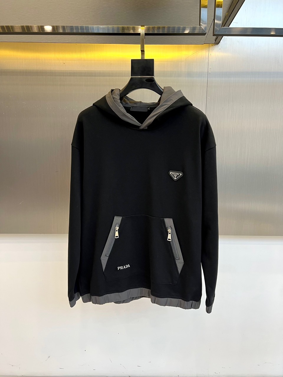 Prad普拉、2025秋冬新作连帽卫衣，款式采用连帽设计搭配可调节抽绳，胸前饰有品牌标志性三角徽标，下方
