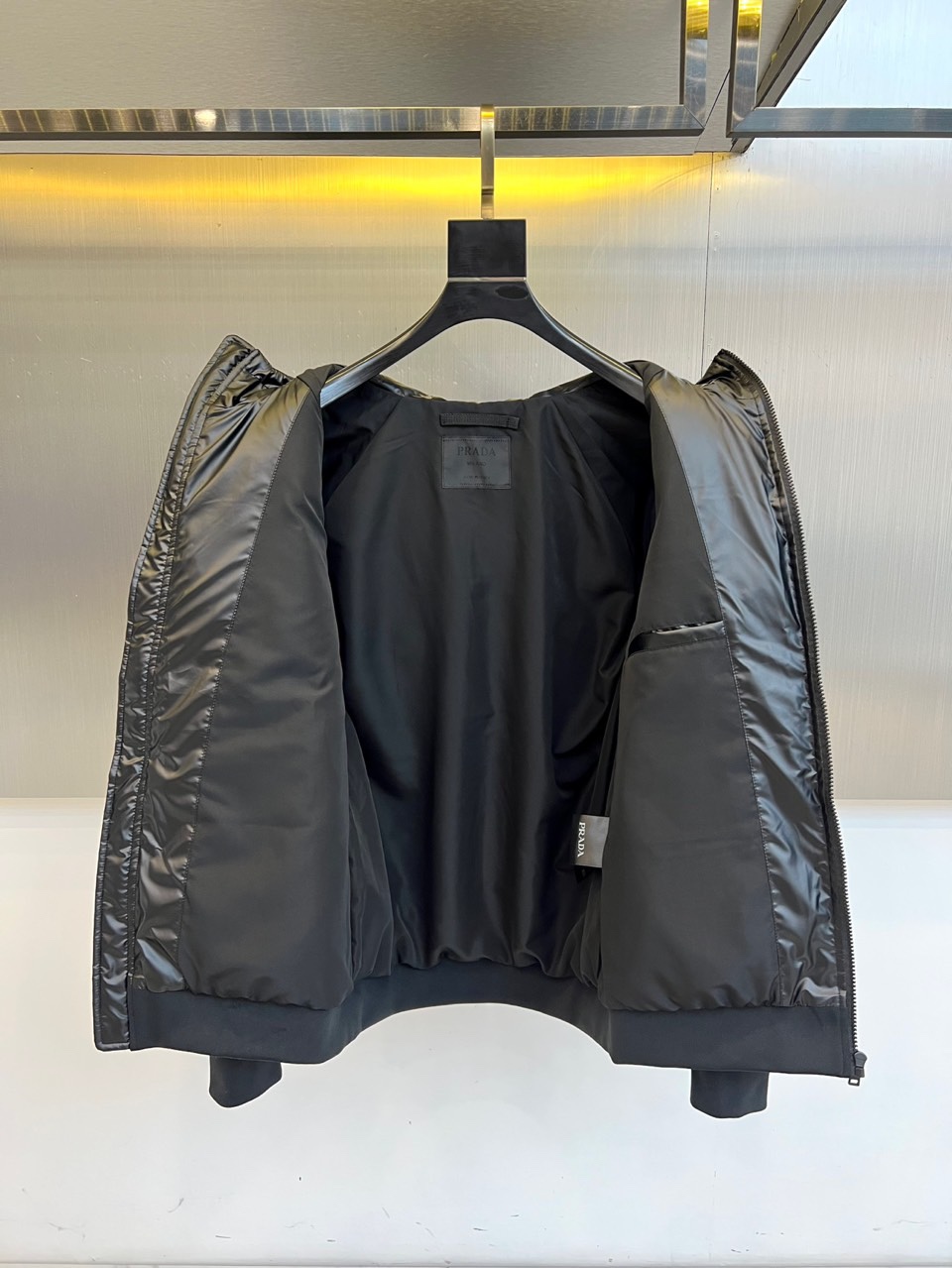 Prad普拉达、2025秋冬新款男士羽绒服，这款连帽羽绒服采用横向绗缝工艺勾勒出饱满的立体轮廓，衣袖部位
