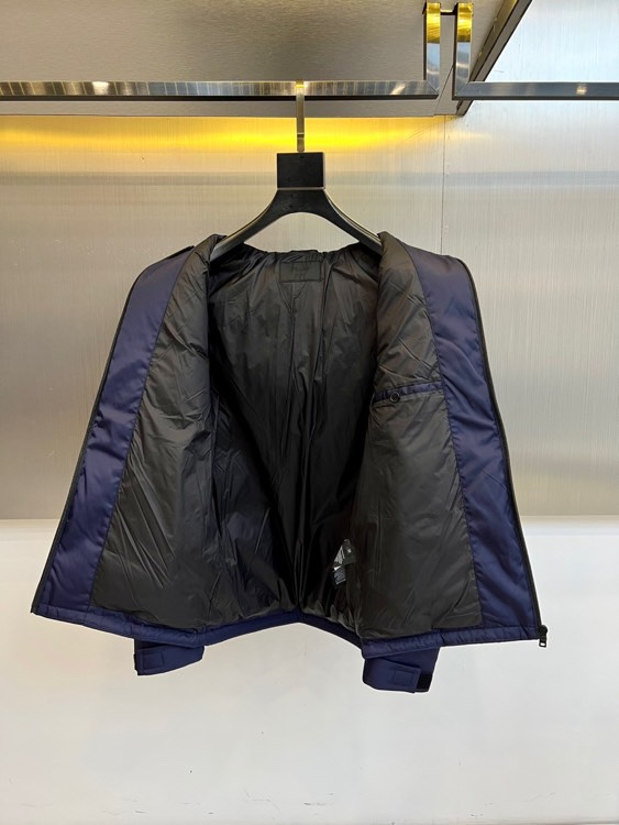 Prad普拉、2025秋冬新品 PRADA科技防护羽绒服。深蓝色连帽设计搭配精密拉链系统，左胸红色织带镶